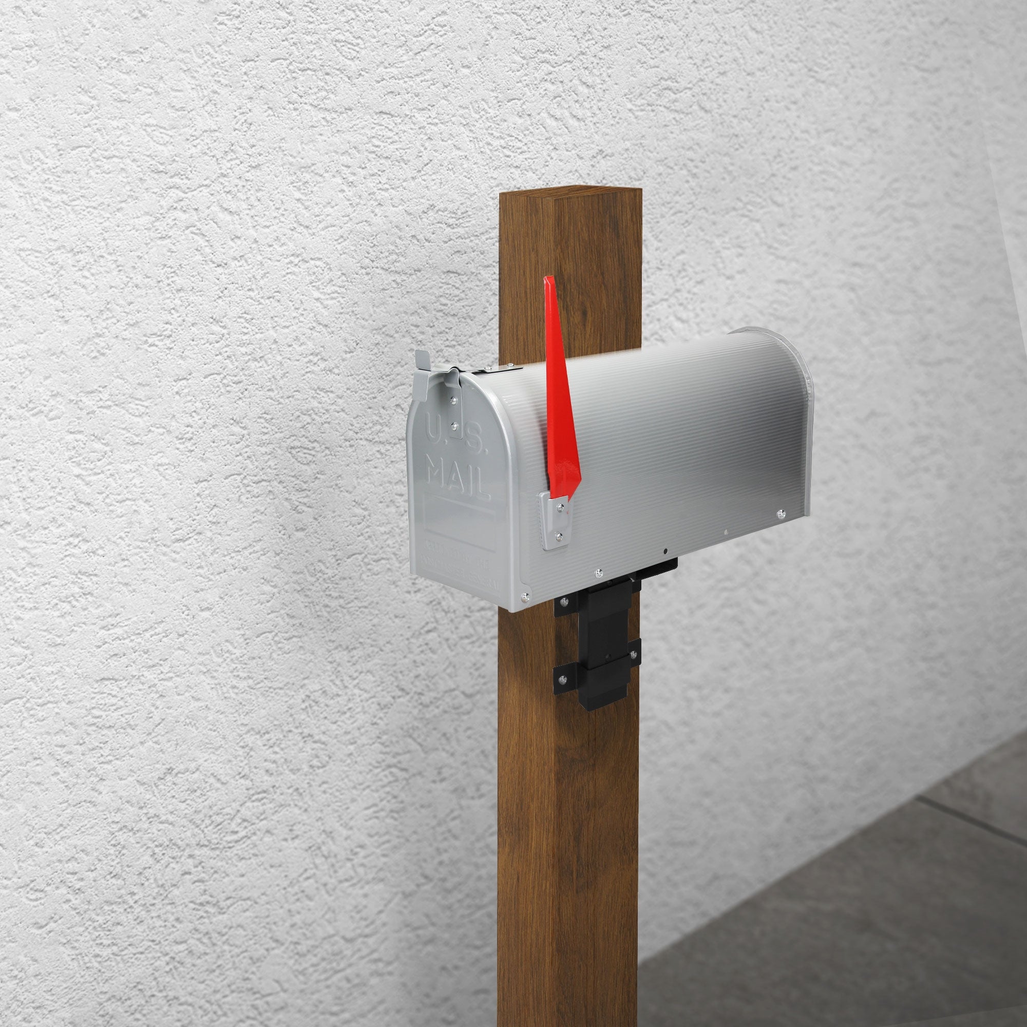 Silver mailbox on a wooden post in front of a white wall.
