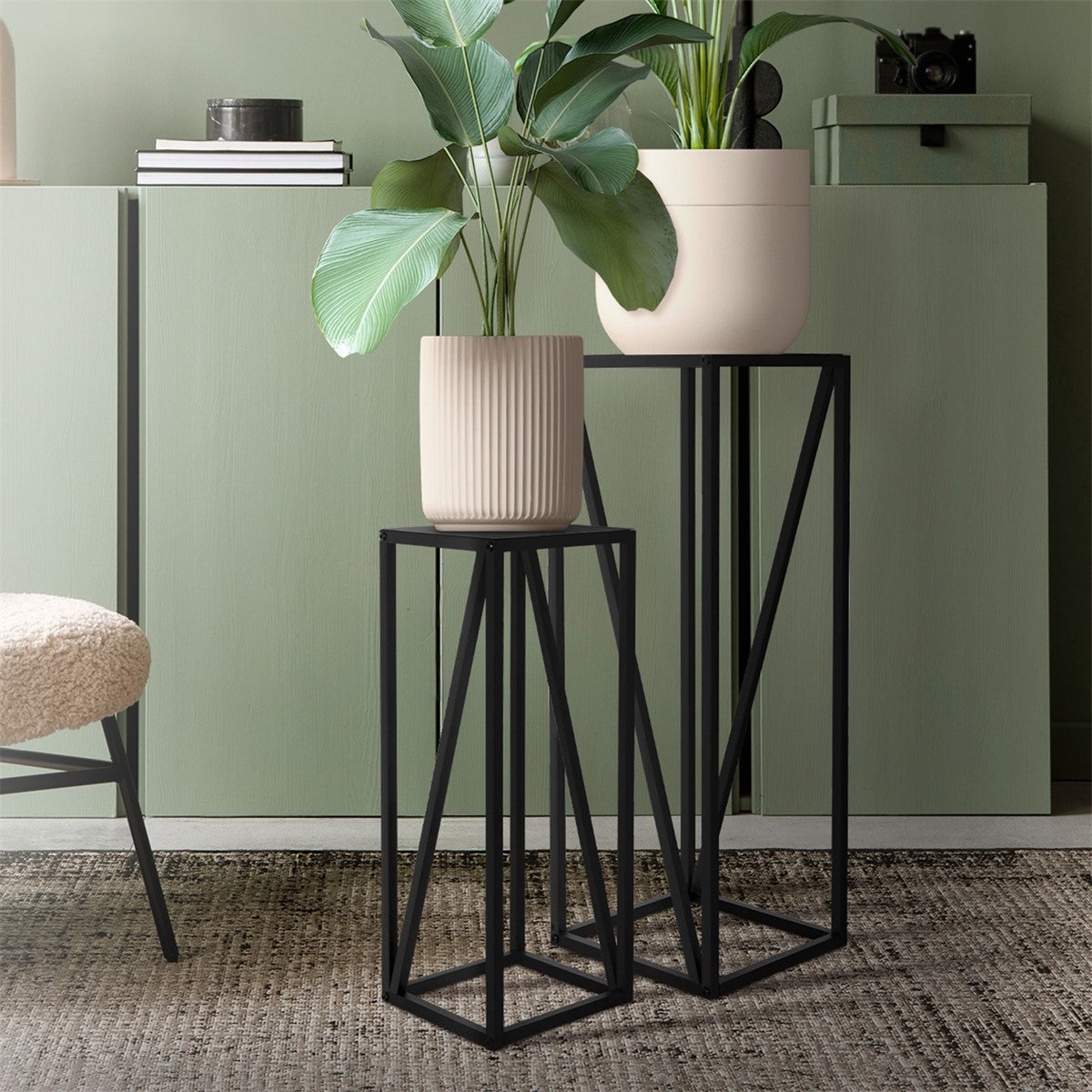 Two plant stands with plants, black frames, in front of a green cabinet.