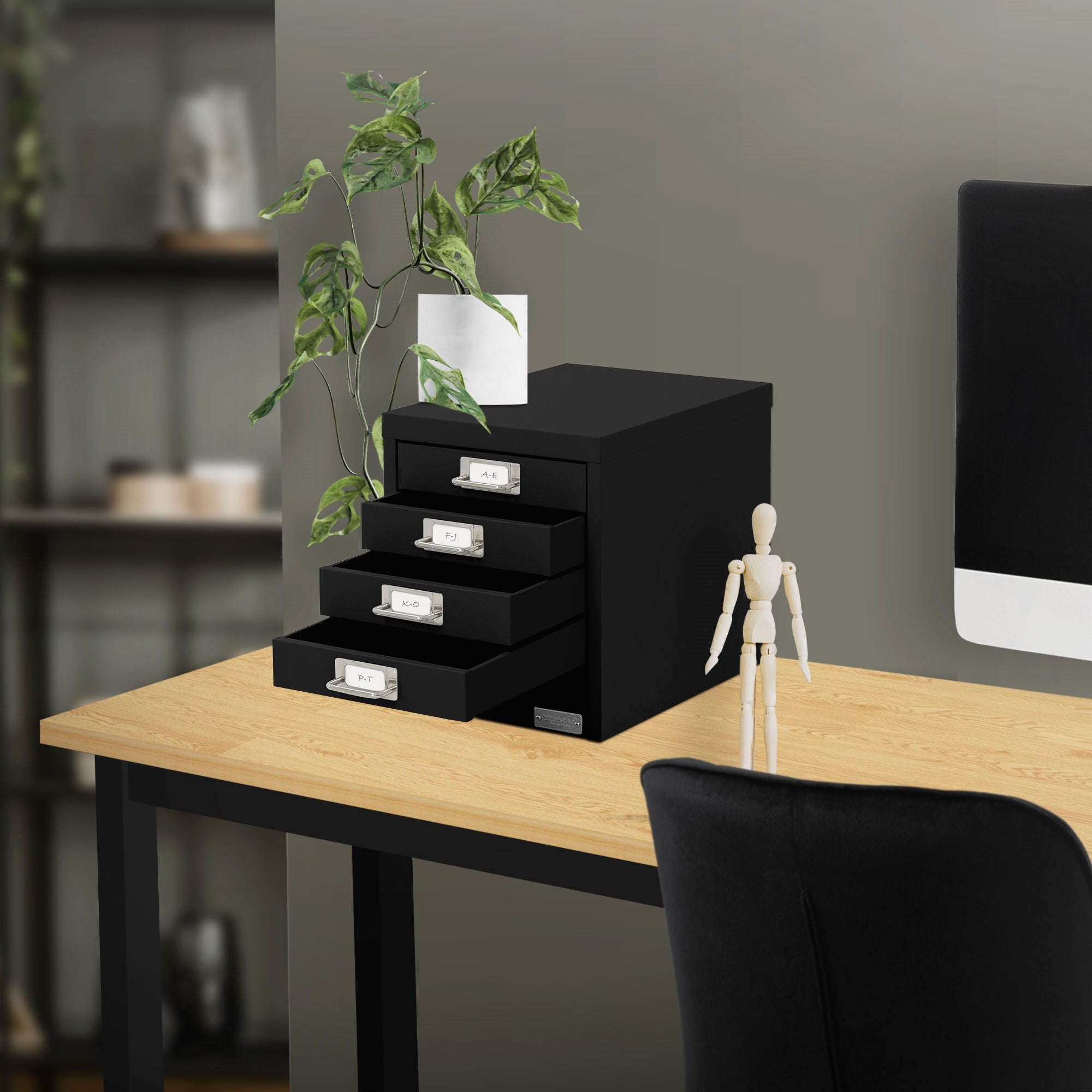 Schreibtisch mit schwarzem Schubladenschrank, Pflanze und Figur.