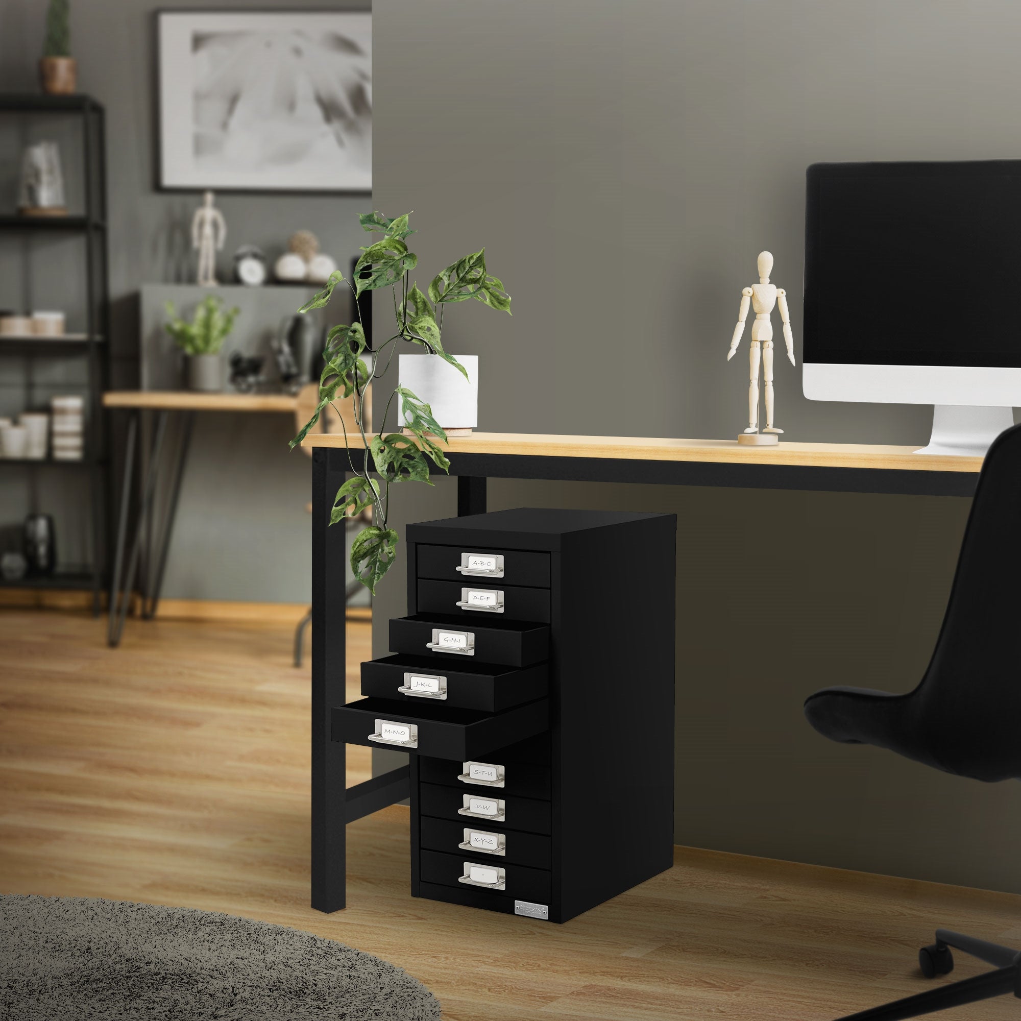 Schreibtisch mit schwarzem Schubladenschrank und Pflanze, daneben ein Computer.