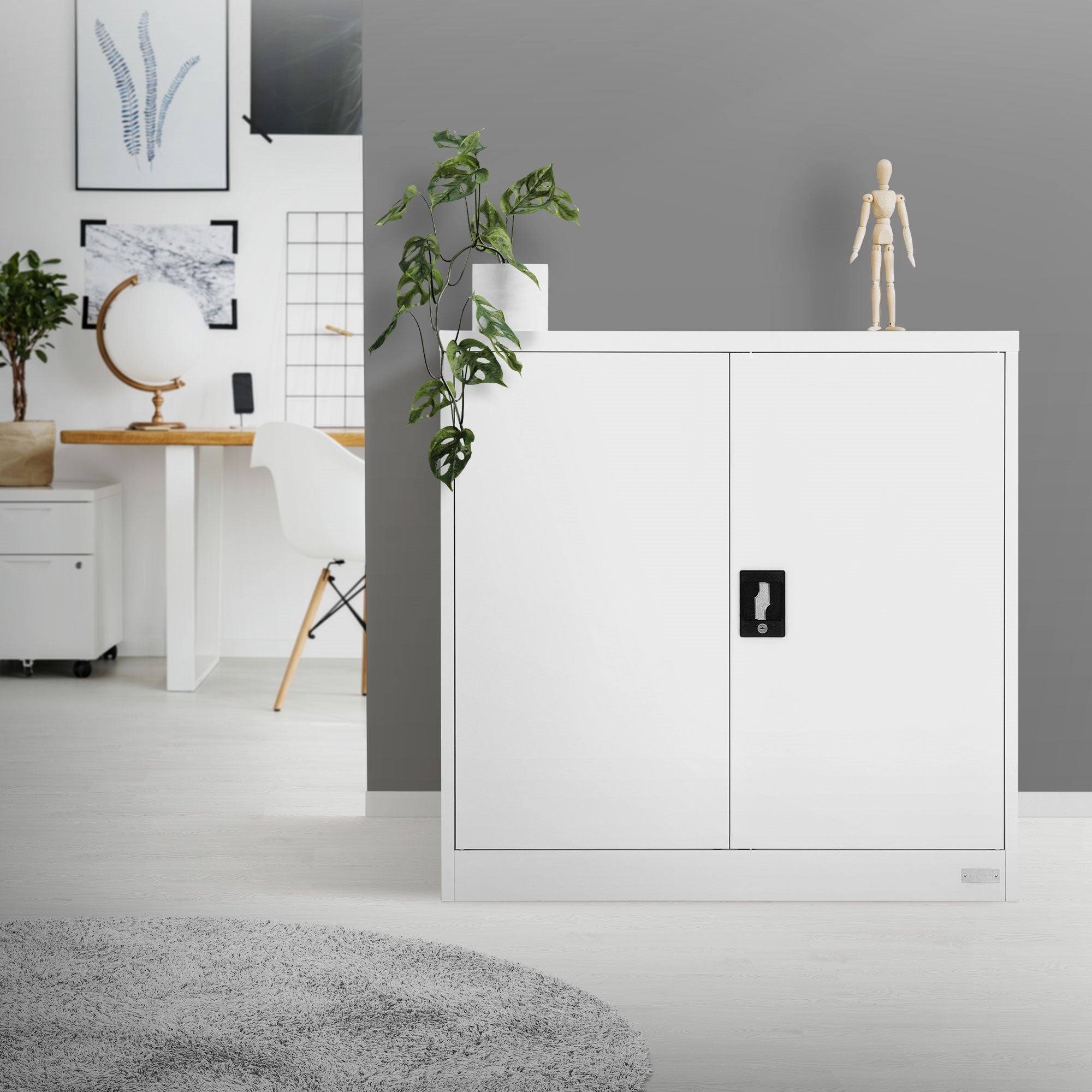Weißer Schrank mit geschlossenen Türen, daneben eine Pflanze und eine Holzfigur.