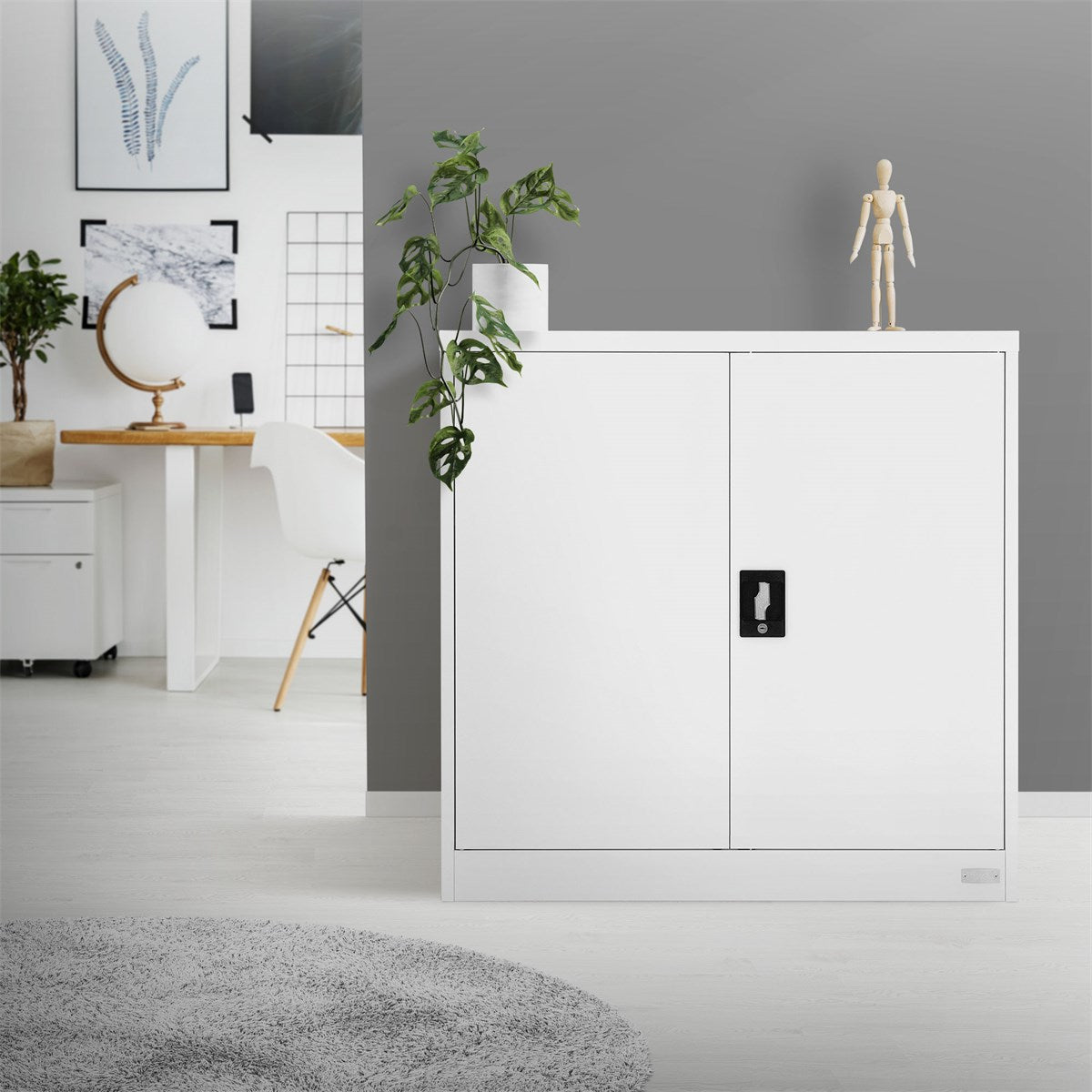 Weißer Schrank mit geschlossenen Türen, daneben eine Pflanze und eine Holzfigur.