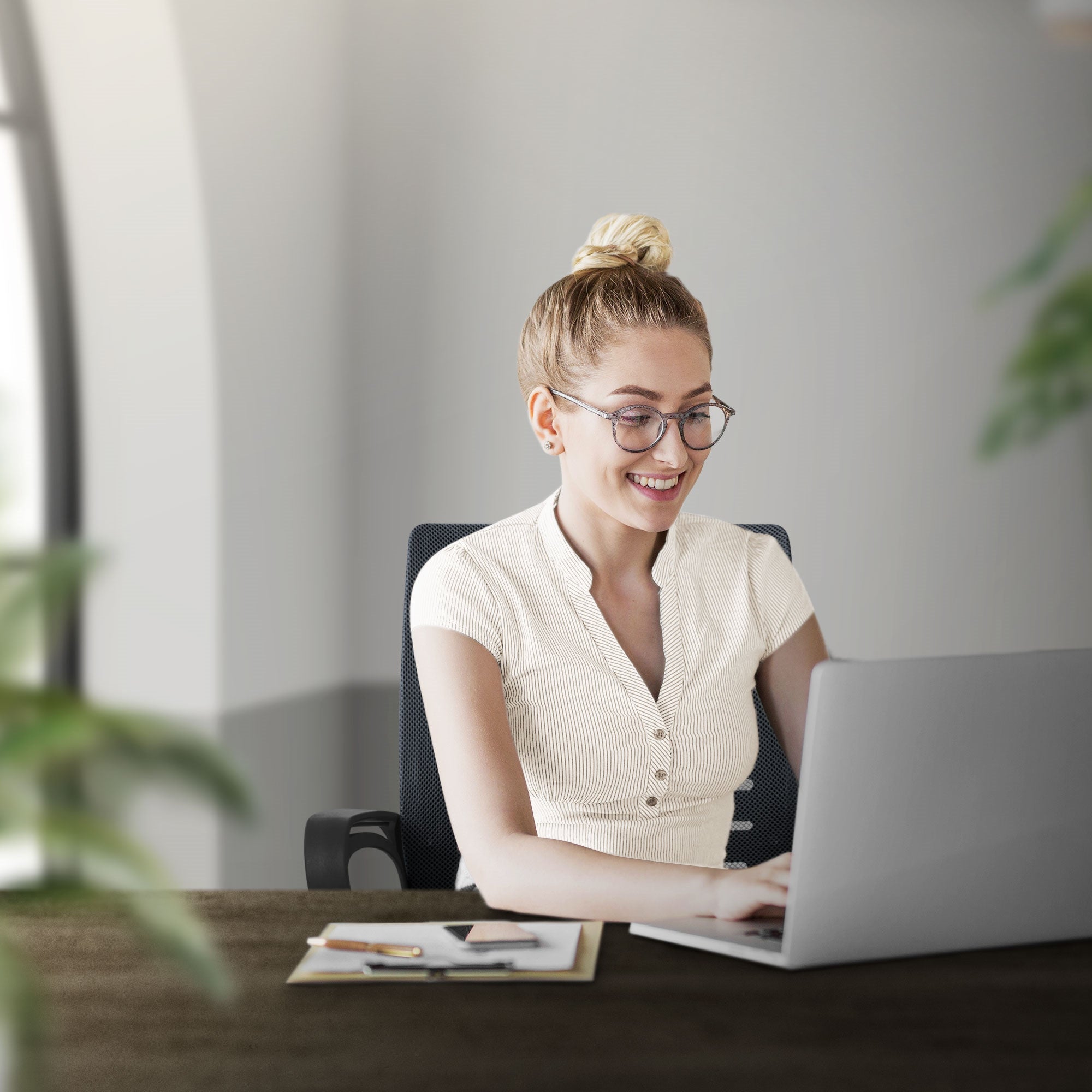 Frau mit Brille sitzt an einem Schreibtisch und arbeitet am Laptop.