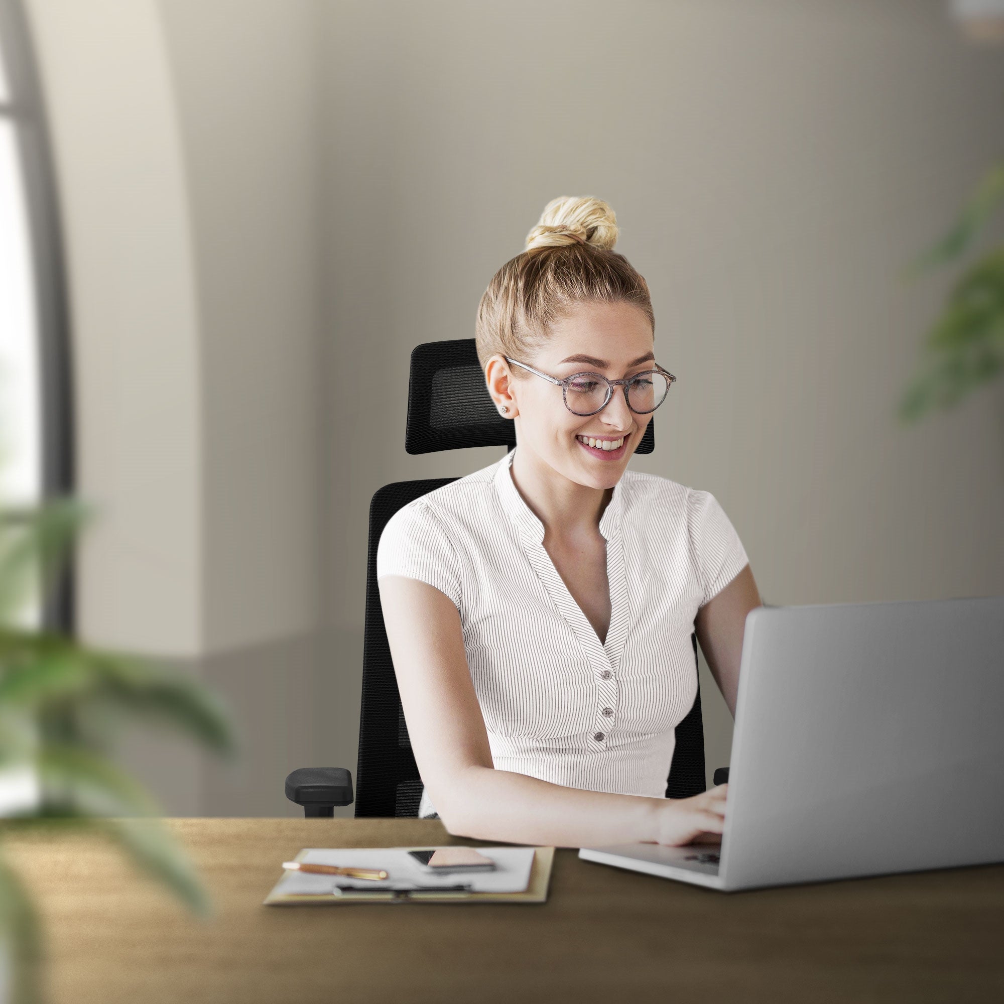 En smilende kvinde sidder ved et skrivebord og arbejder på laptop.
