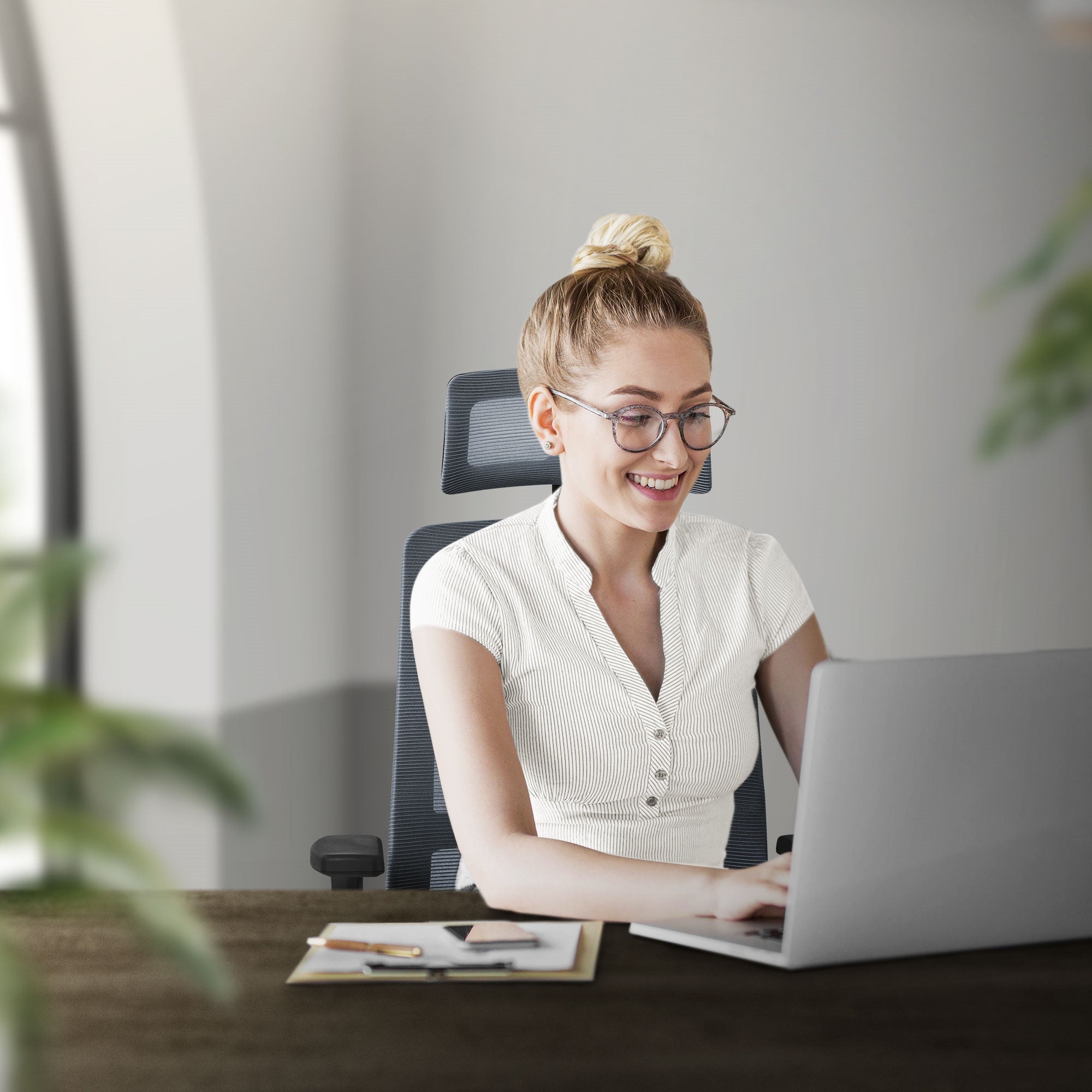 En smilende kvinde sidder ved skrivebordet og arbejder på en bærbar computer.