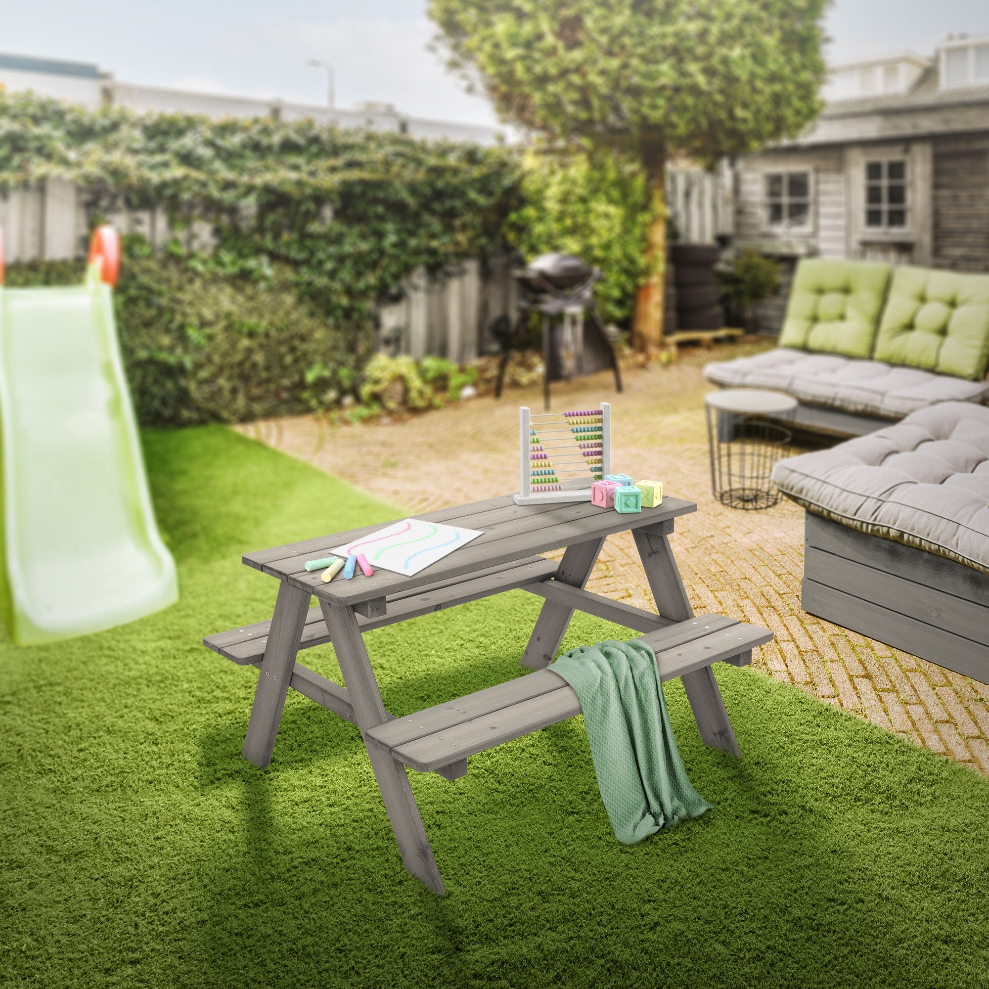 Ein Kindertisch im Garten, dekoriert mit Spielzeug und einer Decke.