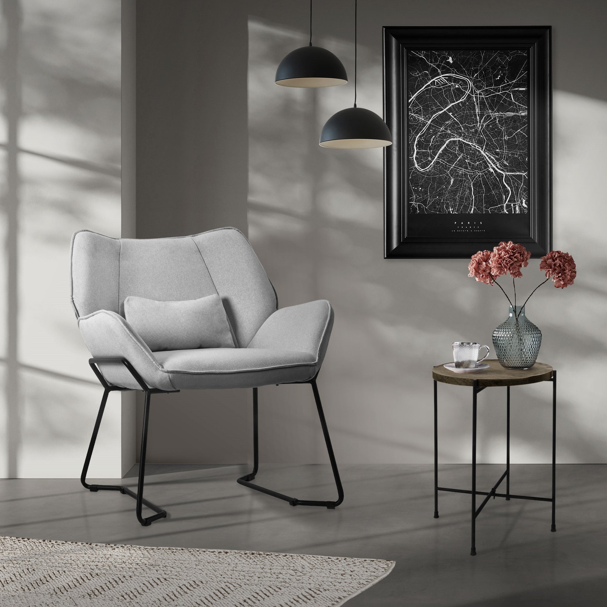 Una poltrona grigia in una stanza con un quadro e un vaso di fiori su un tavolo.