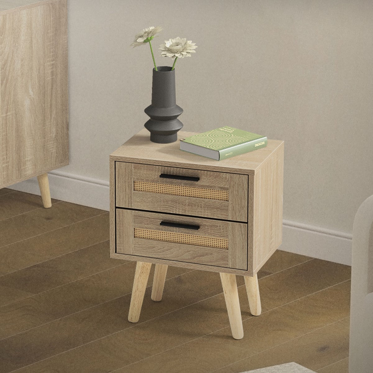 Bedside table with two drawers, a plant and a book on the surface.