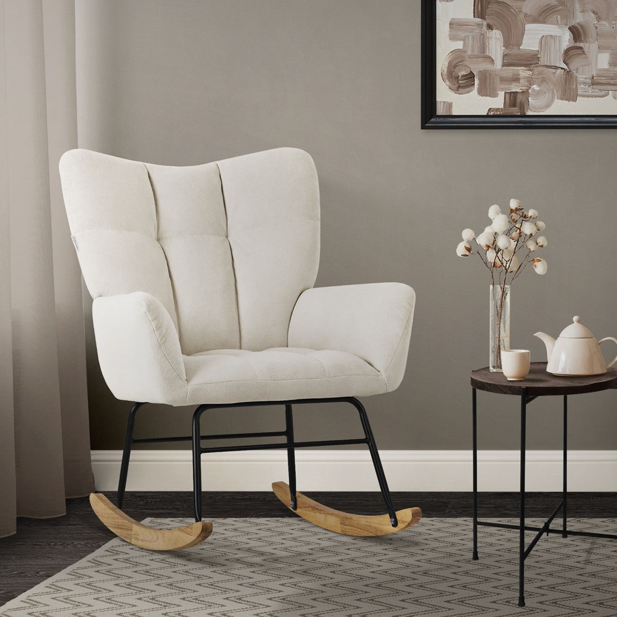 A beige rocking chair in front of a gray wall and a small table with a teapot.