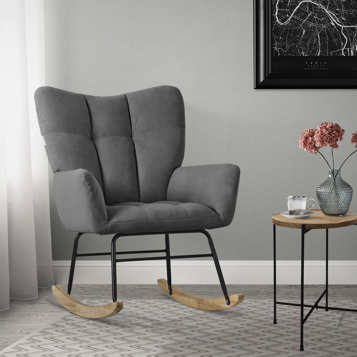 A gray rocking chair beside a table with flowers in a modern room.