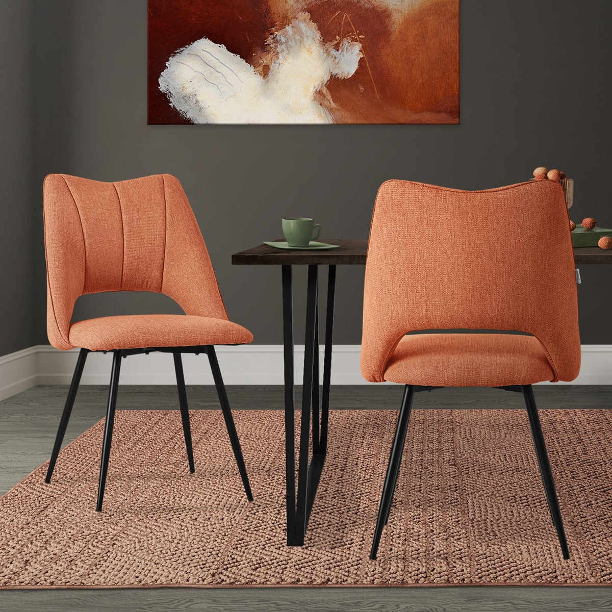Zwei orangefarbene Stühle an einem Tisch in einem Raum mit Kunstwerk.