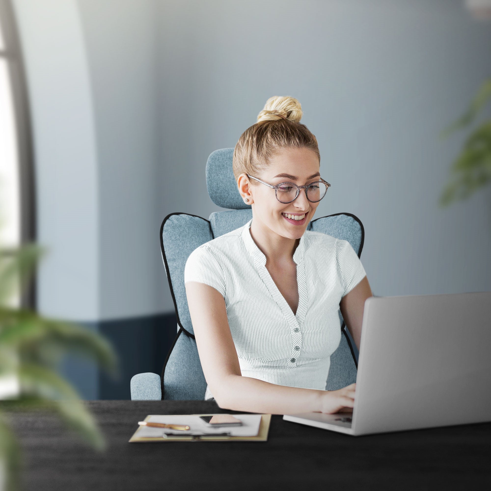 Junge Frau sitzt lächelnd an einem Schreibtisch und arbeitet am Laptop.
