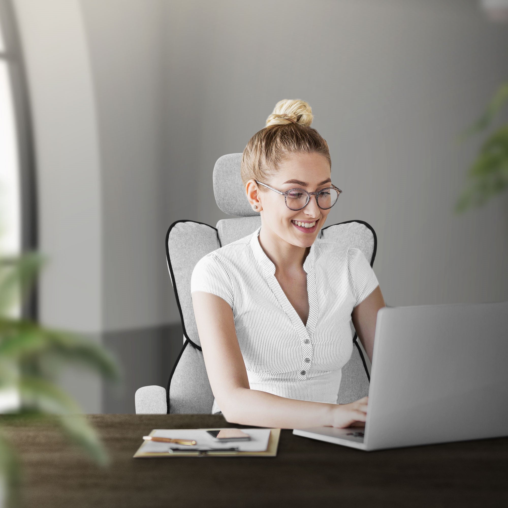 Frau mit Brille sitzt an einem Tisch und arbeitet am Laptop.