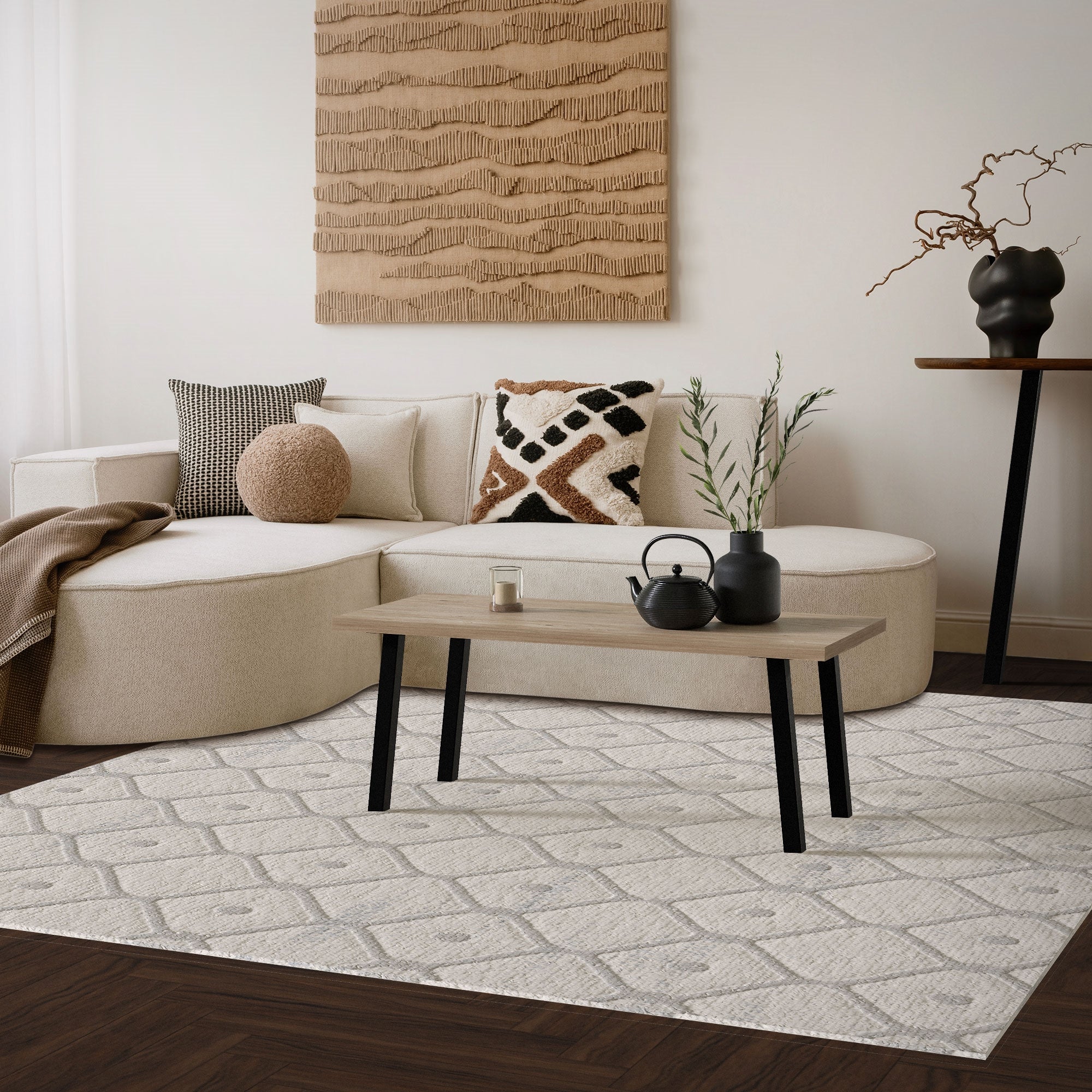 Wohnzimmer mit beiger Couch, Tisch und Teppich, dekoriert mit Pflanzen und Kunstwerk an der Wand.