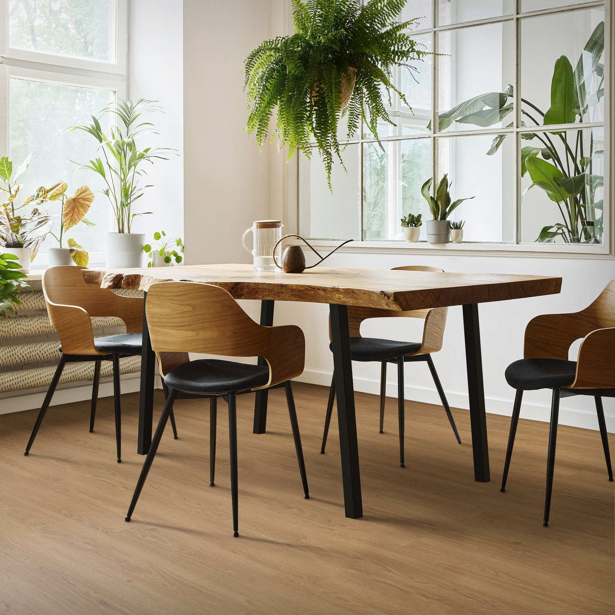 Essbereich mit Holztisch, schwarzen Stühlen und Pflanzen im Hintergrund.