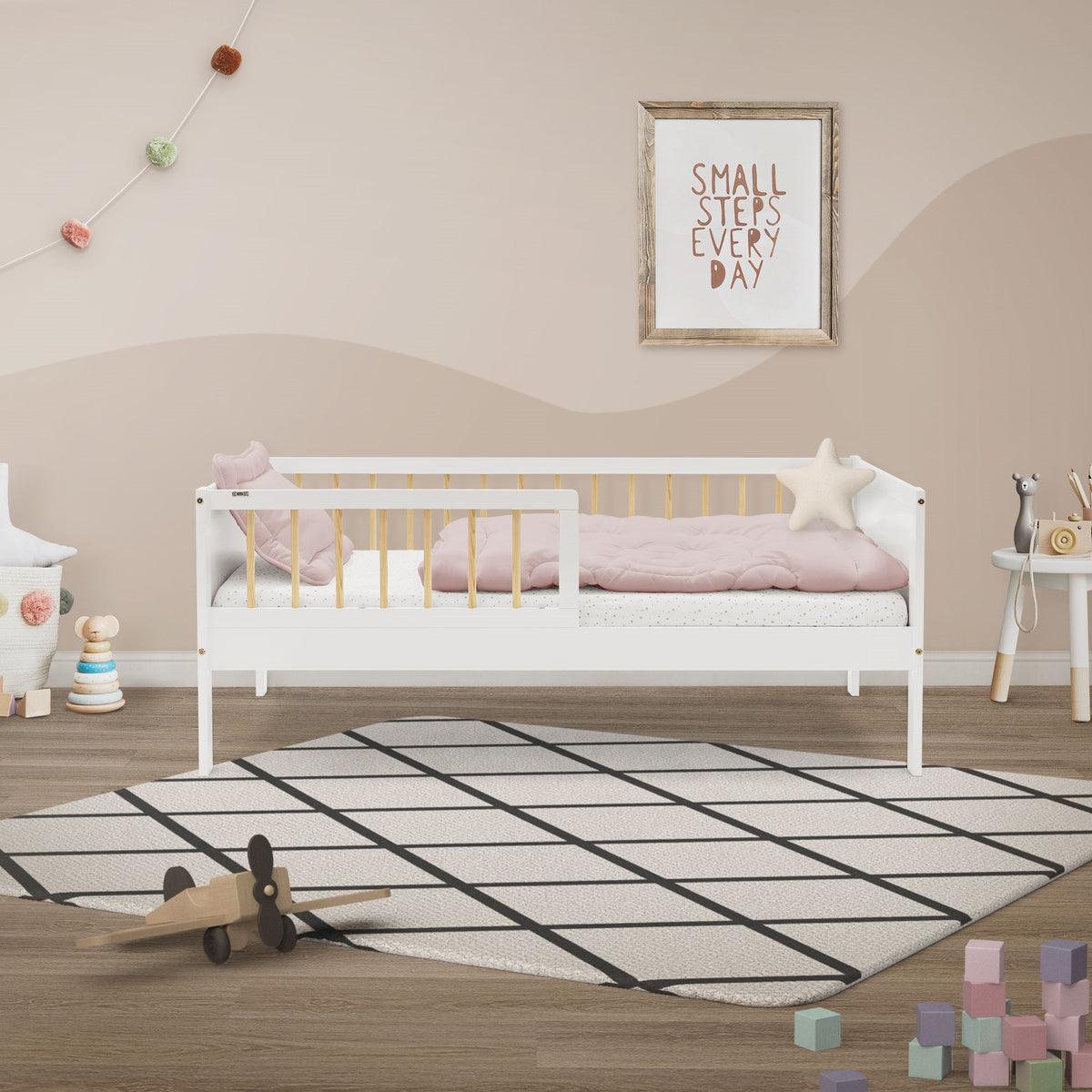 Ein weißes Kinderbett mit rosa Bettzeug und Spielzeug auf dem Boden.