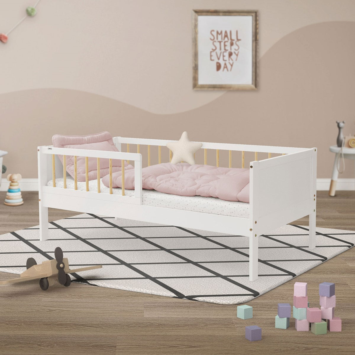 A nursery with a white bed, pillows and toys on the floor.