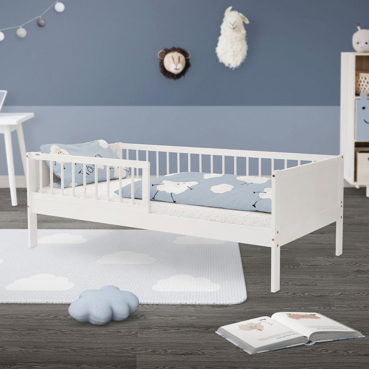 Cama infantil branca num quarto, com roupa de cama com nuvens e brinquedos no chão.