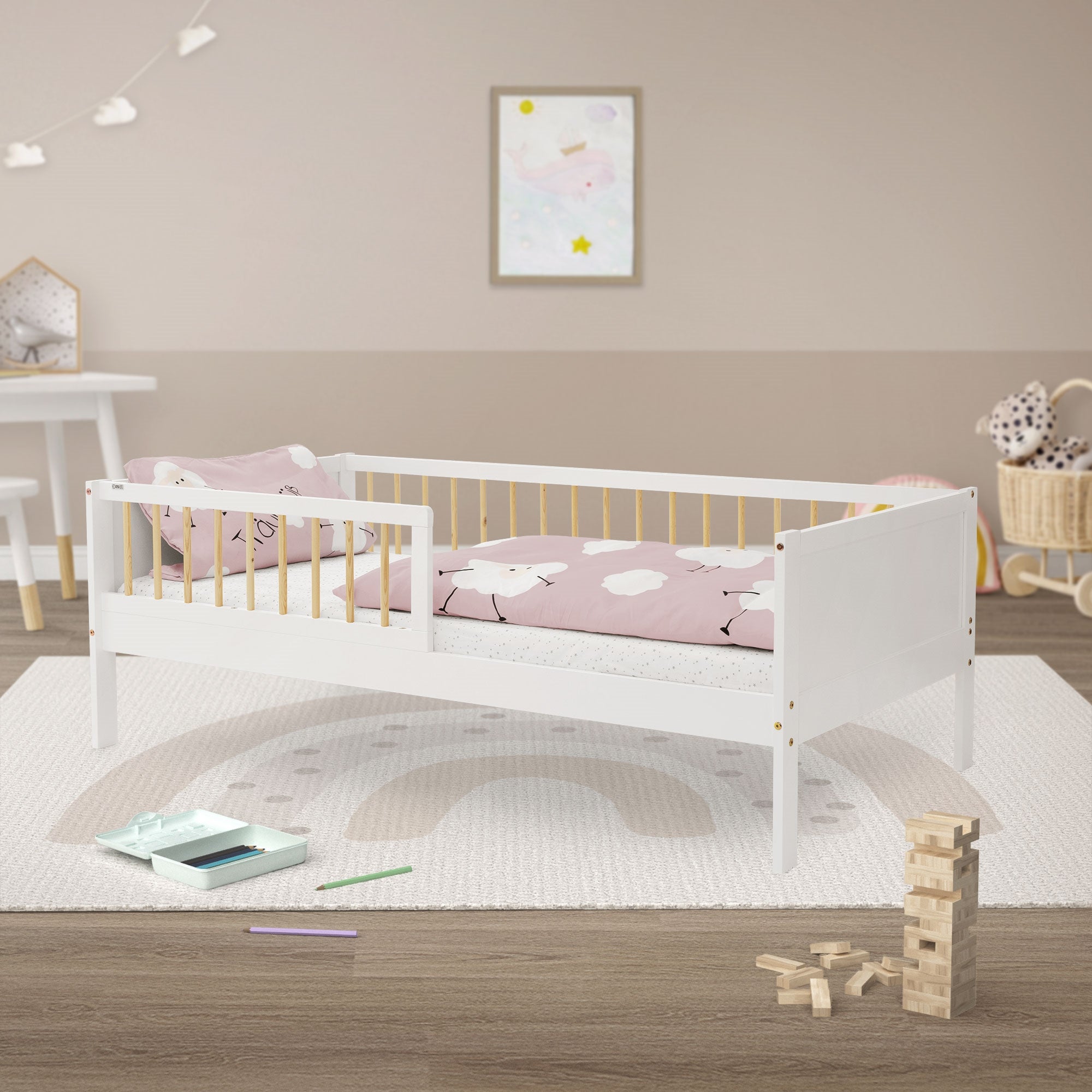 Ein weißes Kinderbett mit rosa Bettwäsche und Spielzeug auf einem Teppich.