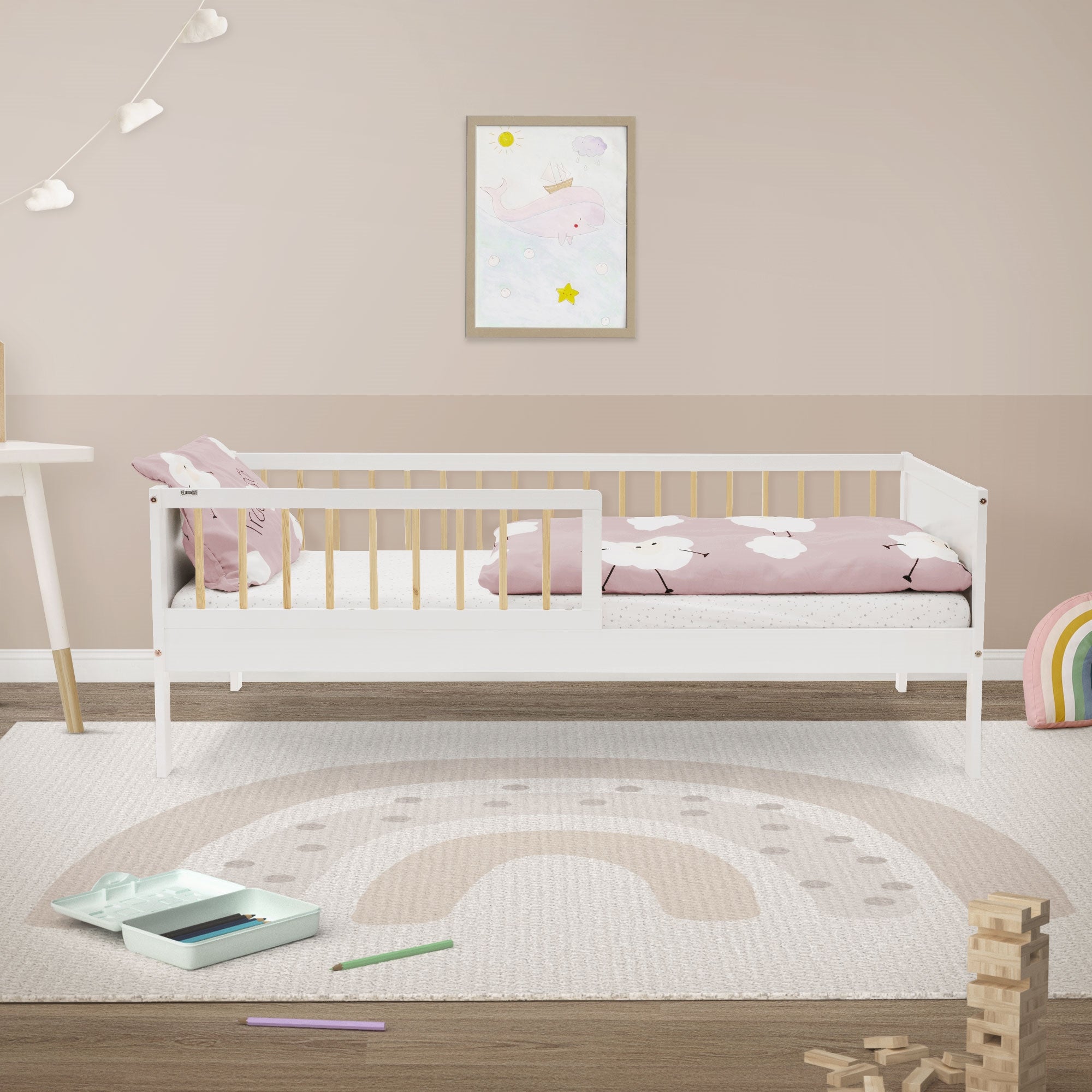 Zimmer mit einem Bett, buntem Bettzeug, Teppich und Spielzeug auf dem Boden.