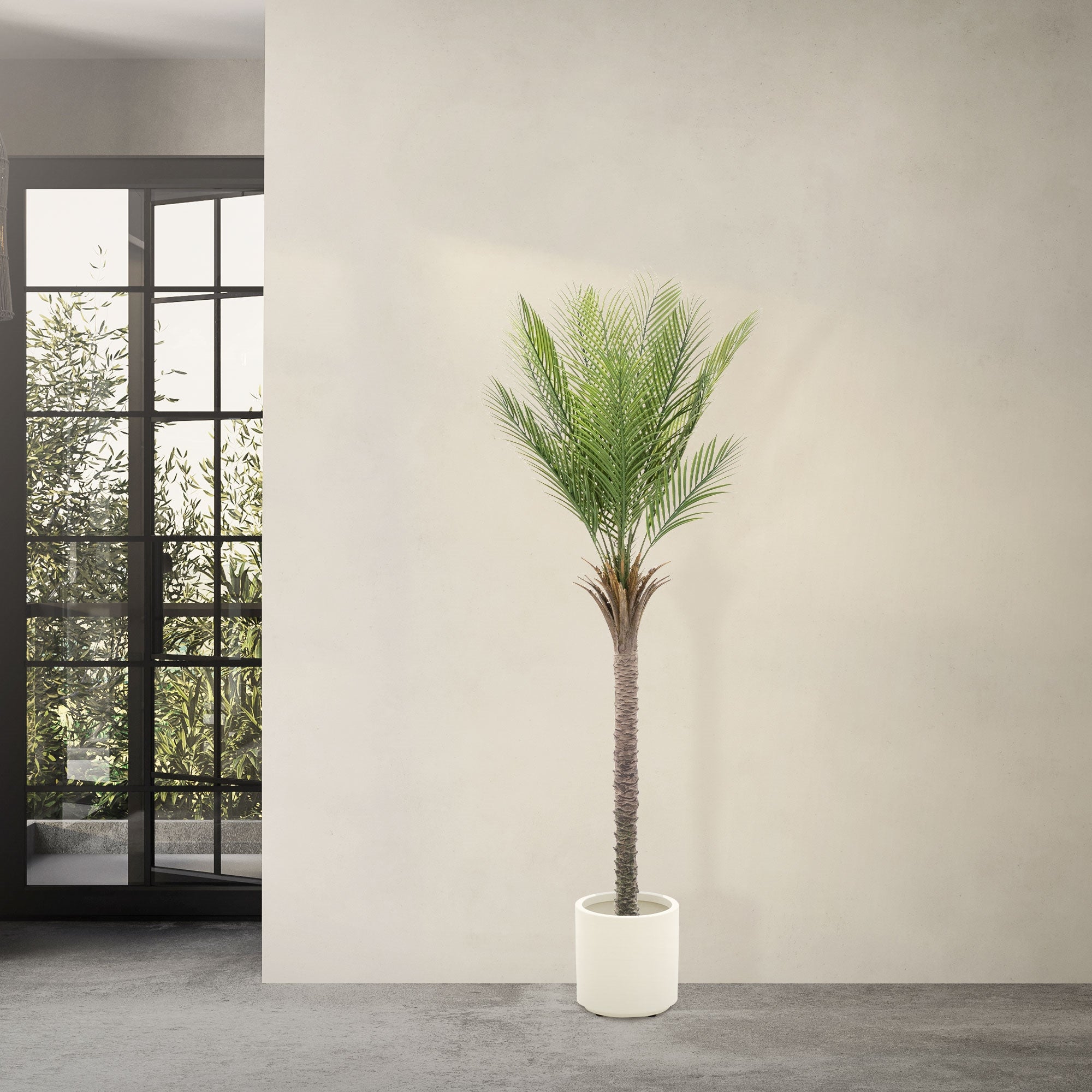 Un albero artificiale in un vaso bianco davanti a una parete grigia e a una finestra.