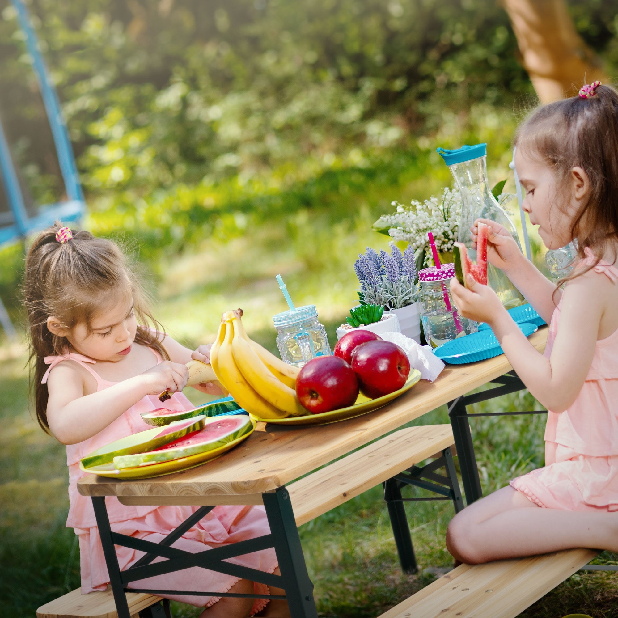 Zwei Mädchen sitzen an einem Tisch im Freien und essen Obst.