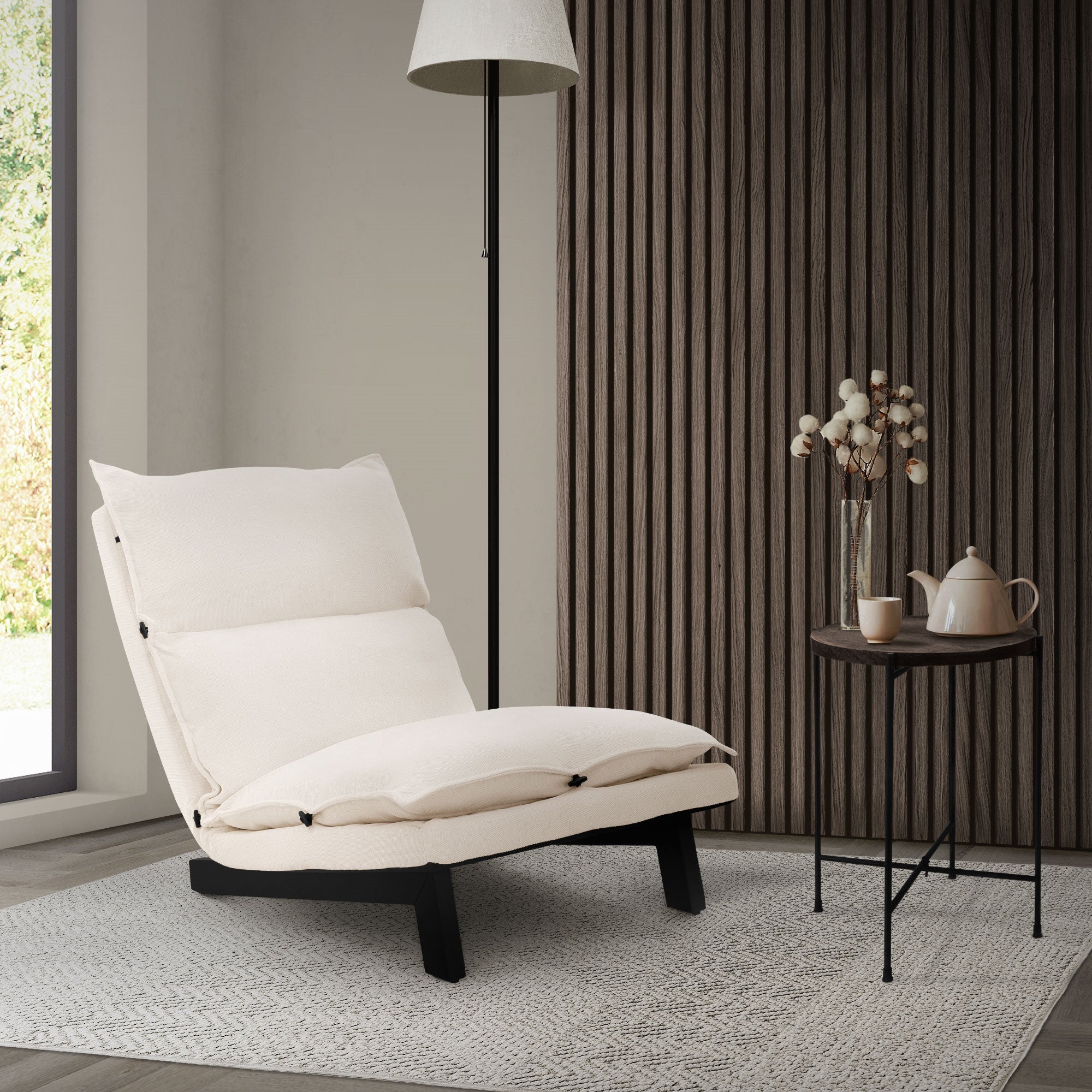 Sillón blanco con almohadas al lado de una mesa y una lámpara en una habitación luminosa.