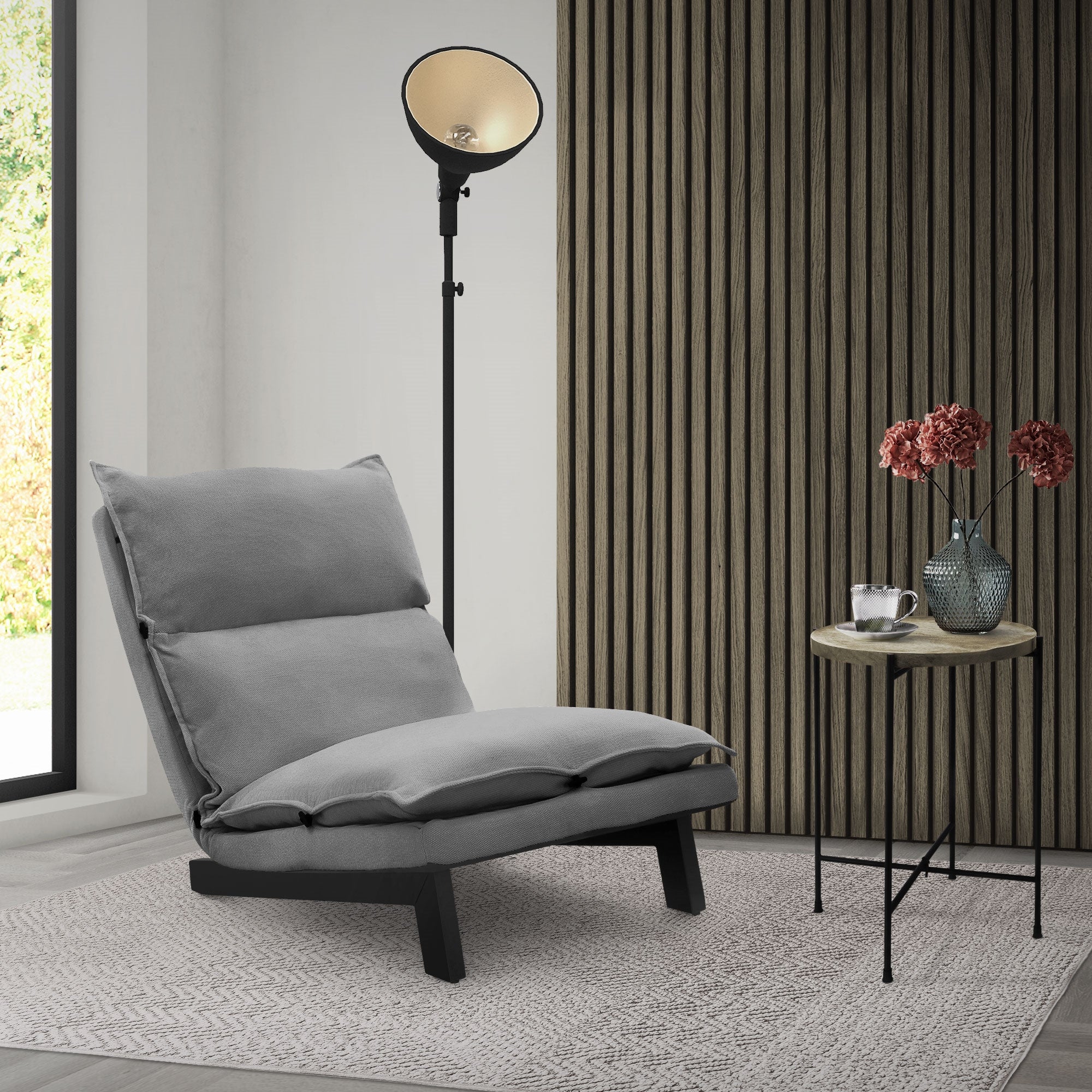 Sillón gris cómodo al lado de una mesa con flores y una lámpara.