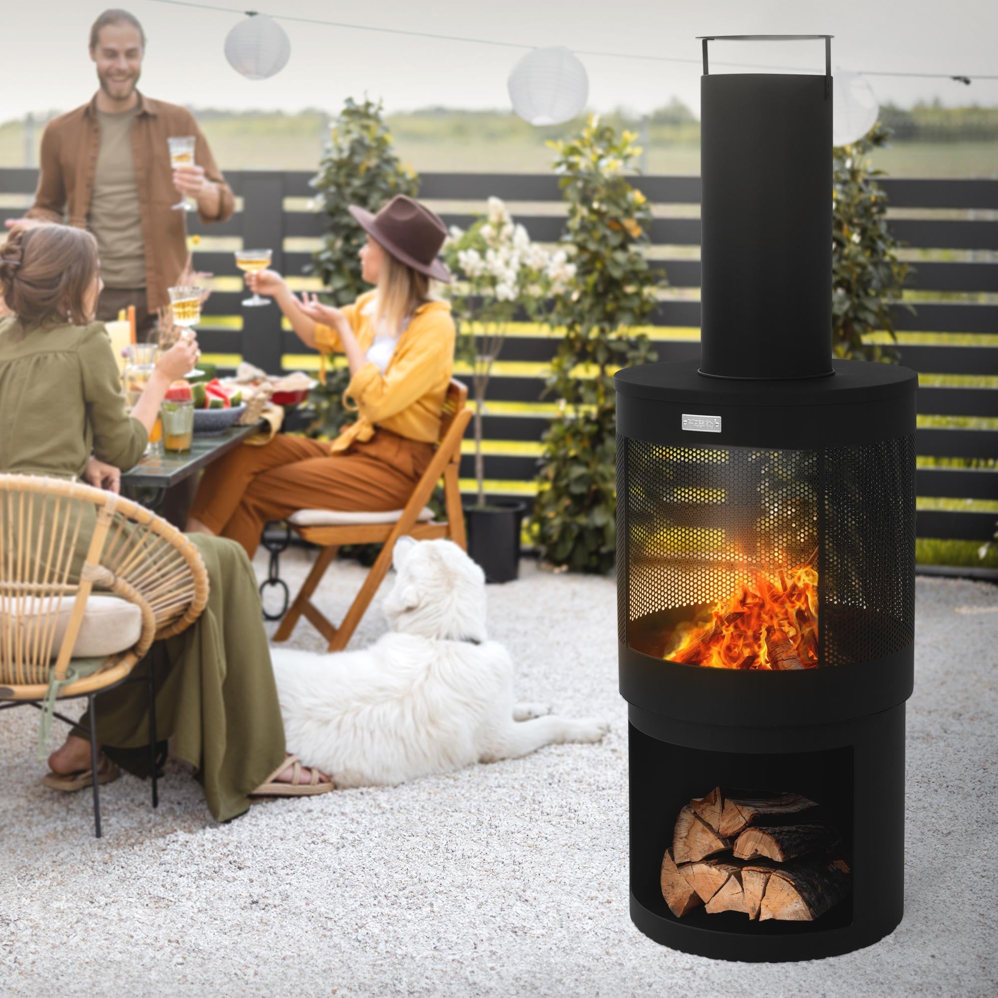 Eine Gruppe von Menschen sitzt um einen Gartenkamin mit Feuer, umgeben von Pflanzen.