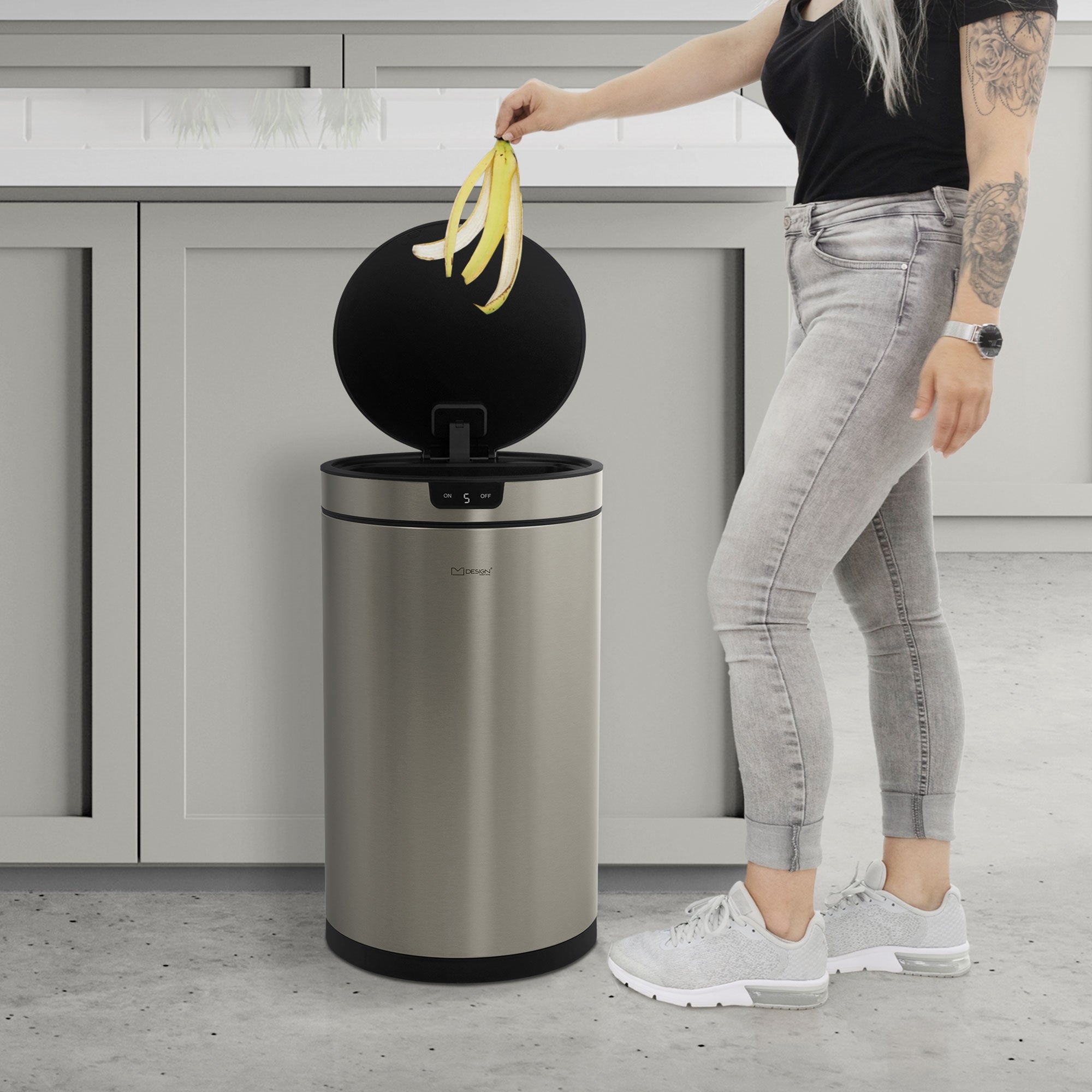 Person mit langen Haaren, die Bananen in einen Edelstahl-Mülleimer wirft.