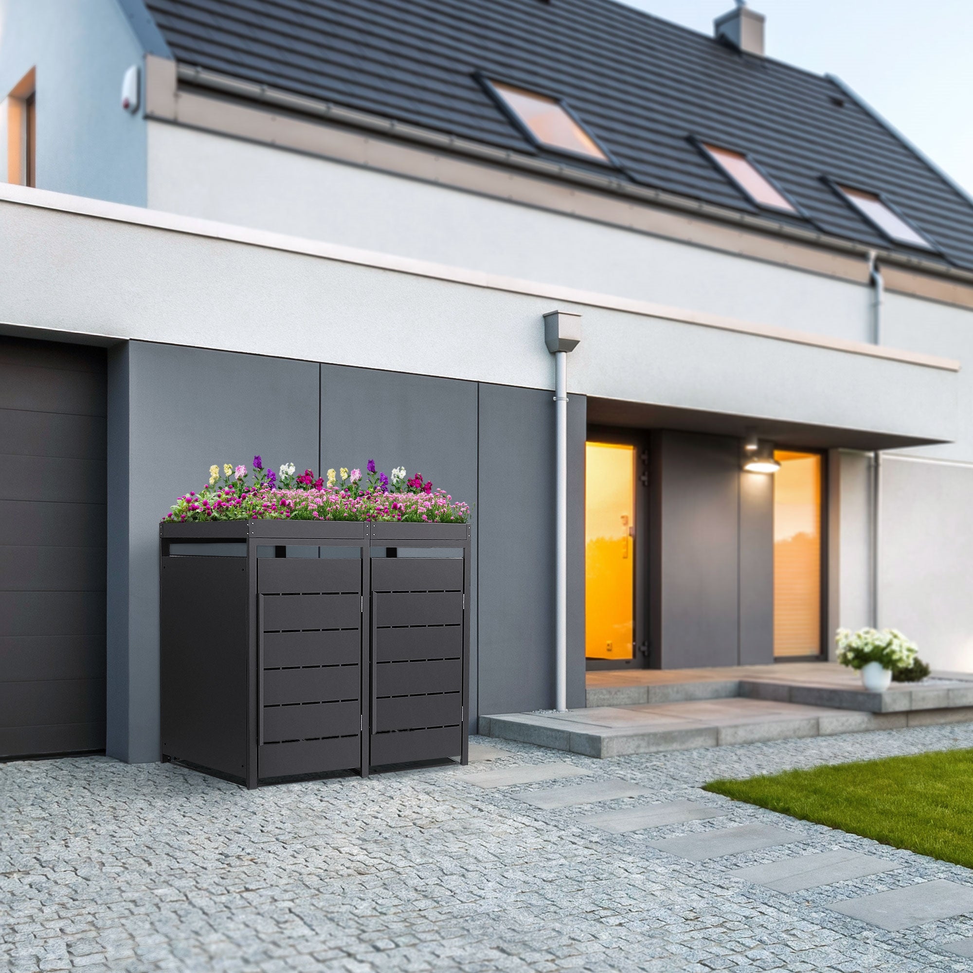 Mülltonnenbox mit Blumen bepflanzt, vor einem modernen Haus.