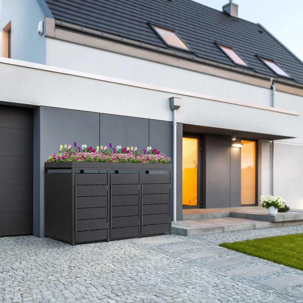 Drei Abfallbehälter mit Blumen auf einem modernen Hausvorplatz.