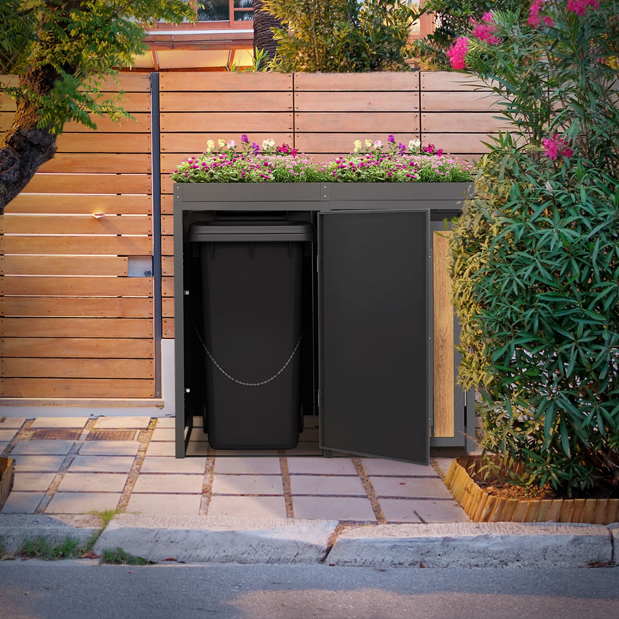 Boîte à poubelles avec des plantes, située sur un chemin entre des arbres.