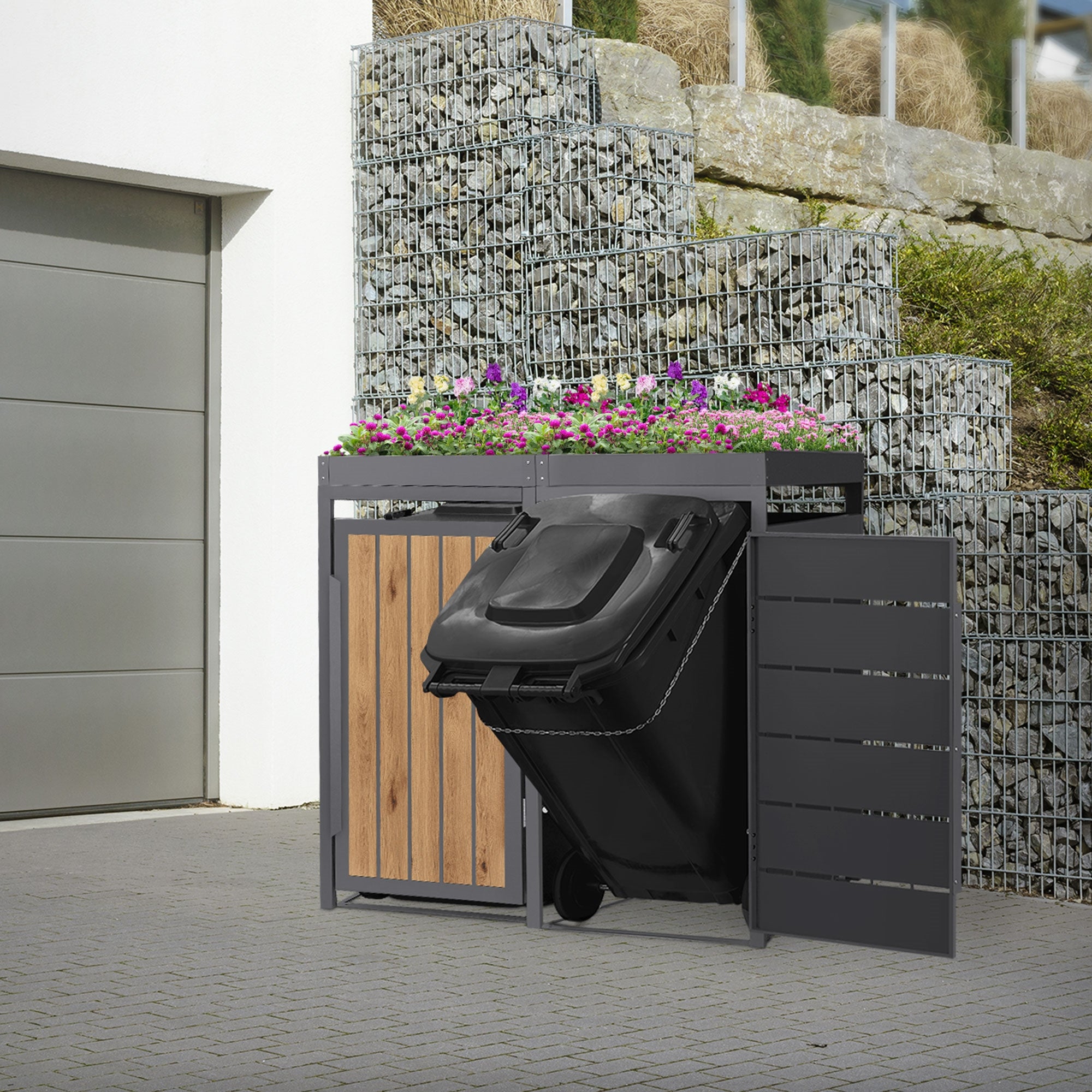 Poubelles avec arrangement de plantes, à côté d'un mur en pierre.