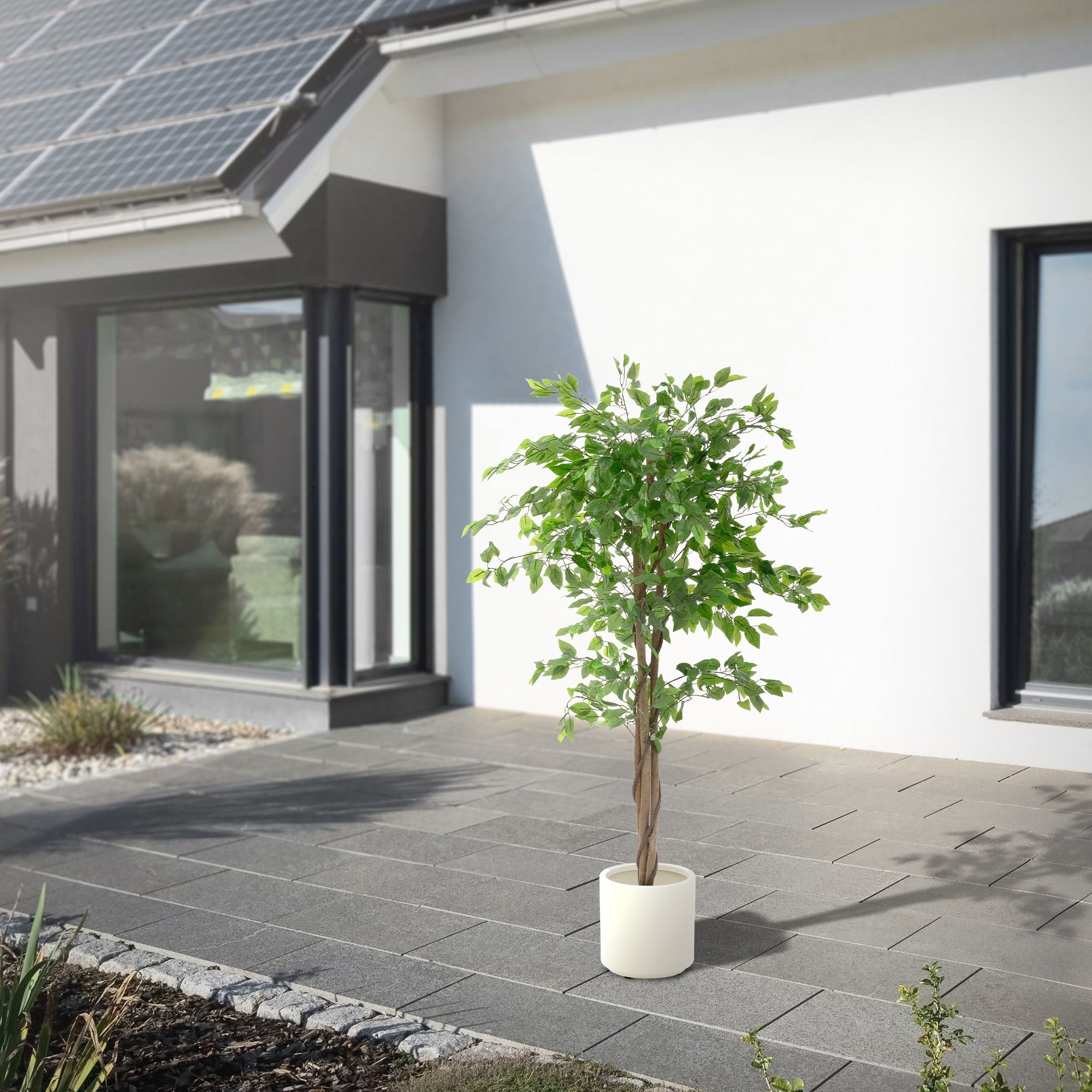 Un albero artificiale in un vaso bianco davanti a una casa moderna.