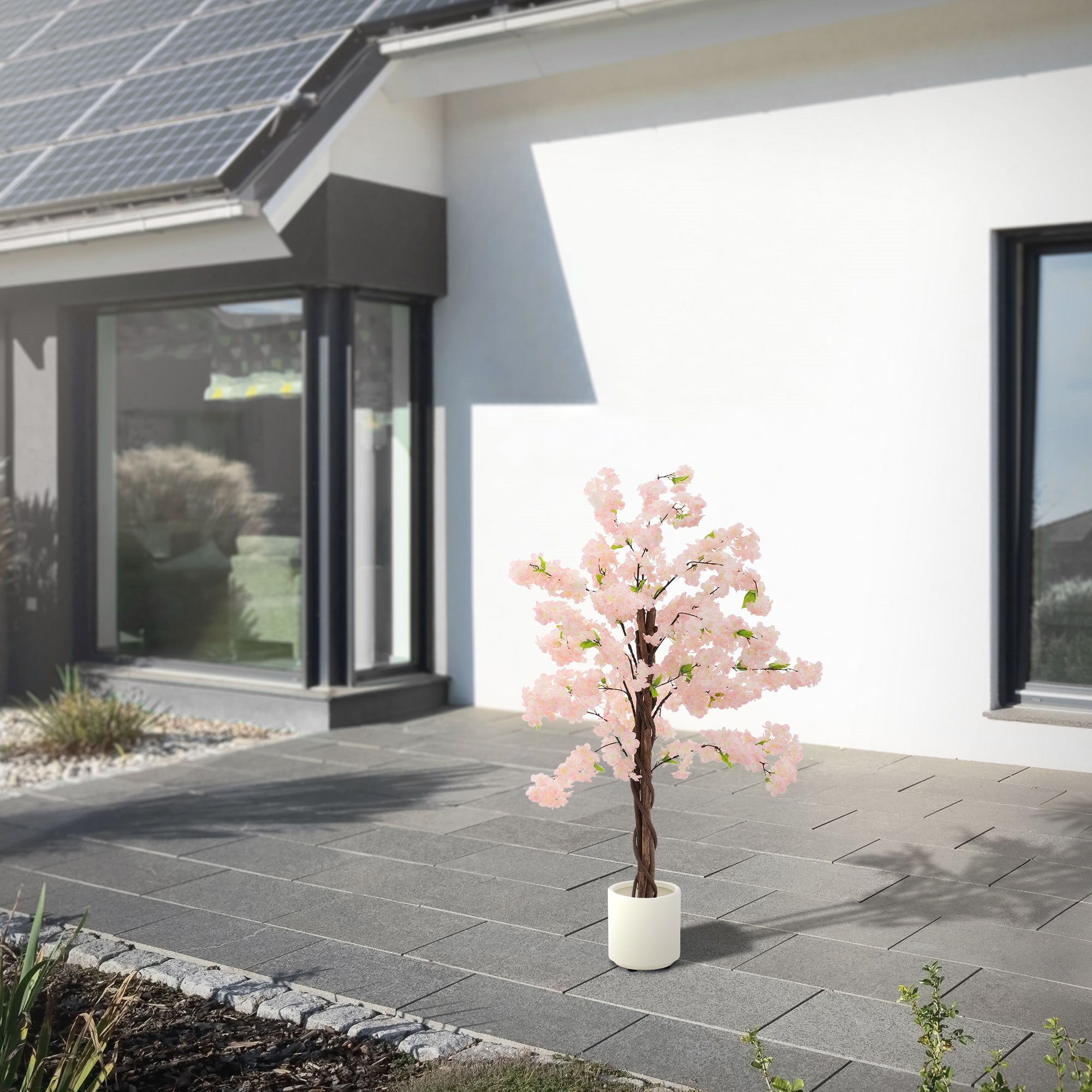 Albero artificiale con fiori rosa davanti a una casa moderna con pannelli solari.