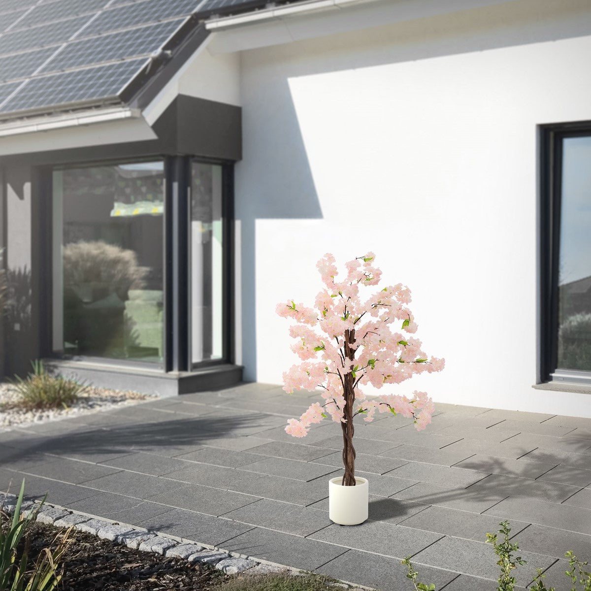Albero artificiale con fiori rosa davanti a una casa moderna con pannelli solari.