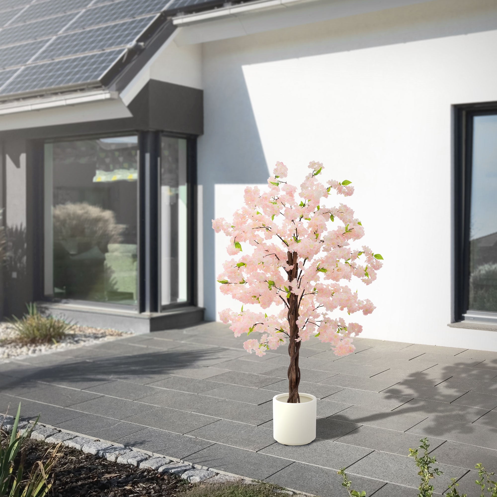 Albero artificiale con fiori rosa davanti a una casa moderna con pannelli solari.