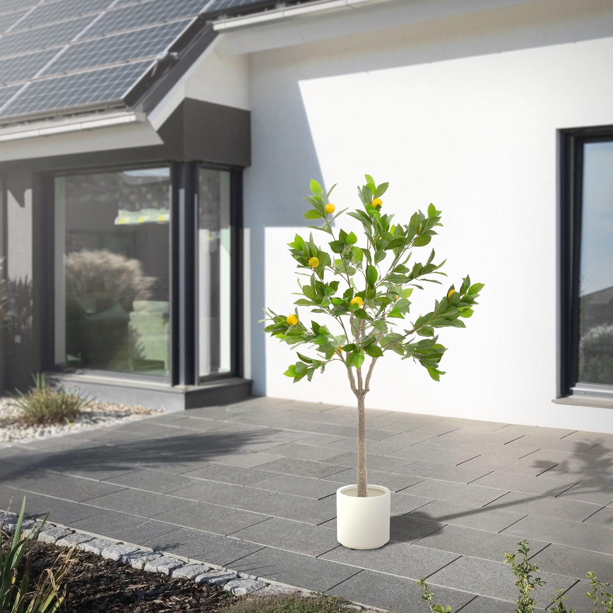 Künstlicher Baum mit Zitronen in einem Topf, auf einer Terrasse vor einem Haus.