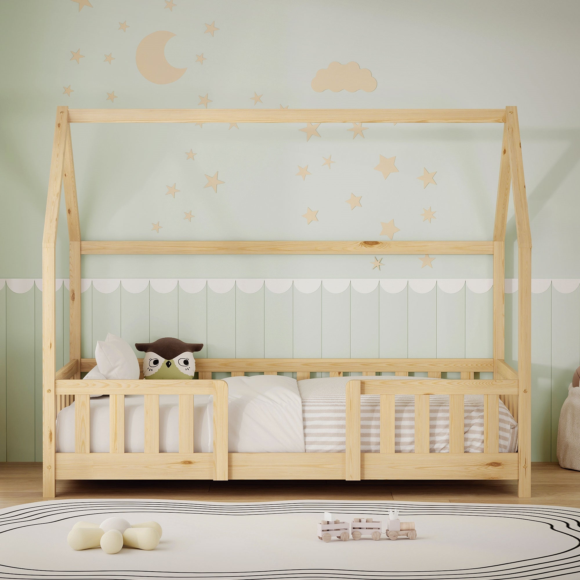 Cuna de estructura de madera con forma de techo, almohada y juguetes sobre el colchón, pared con luna y estrellas.