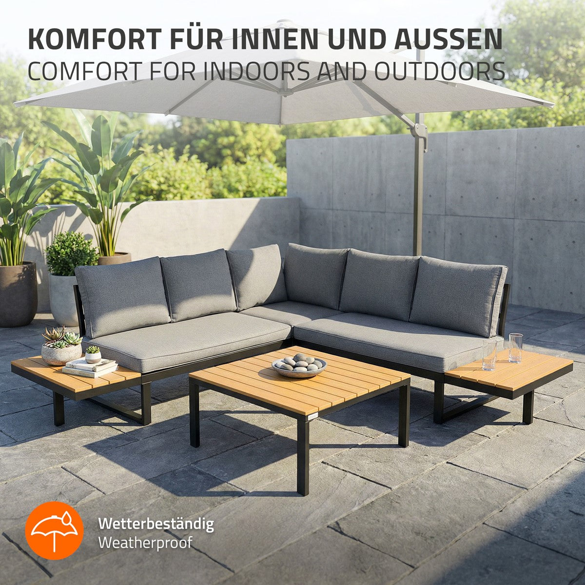 Sitzgruppe aus grauem Stoff und Holz auf einer Terrasse mit Pflanzen im Hintergrund.