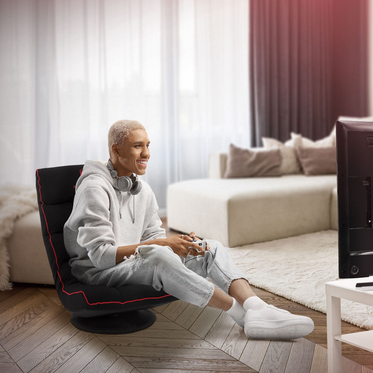 Junger Mann sitzt auf einem Sessel und spielt Videospiele vor einem Fernseher.
