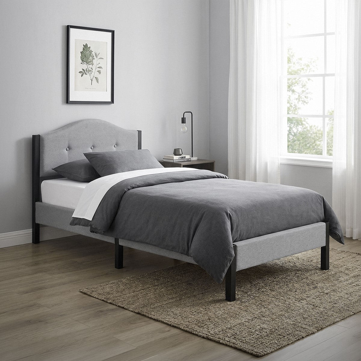 Gray bed with bedding and bedside table in a bright setting.