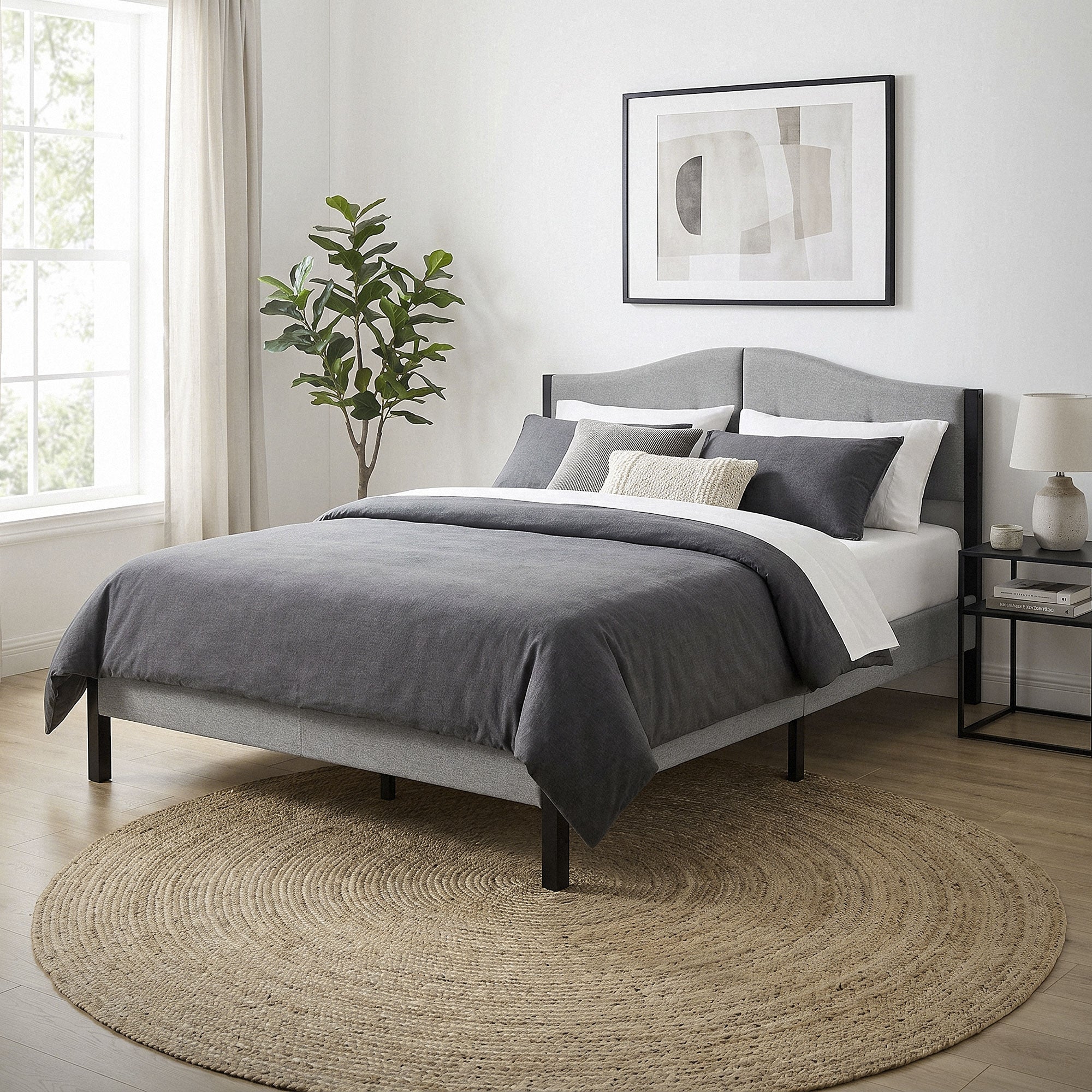 Schlafzimmer mit einem grauen Bett, Kissen und einem runden Teppich.
