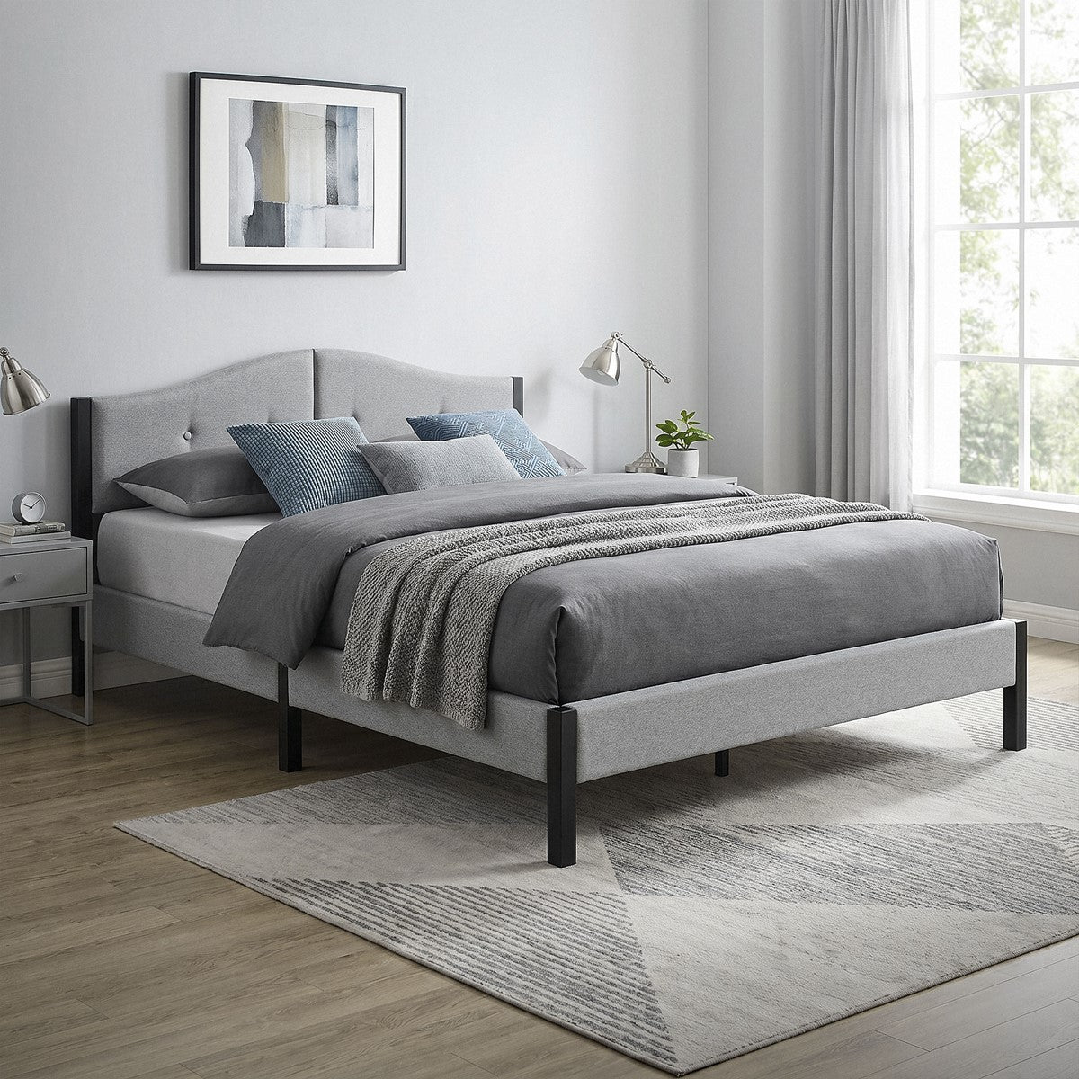 Letto con rivestimento grigio, cuscini e copriletto, finestra con tende sullo sfondo.