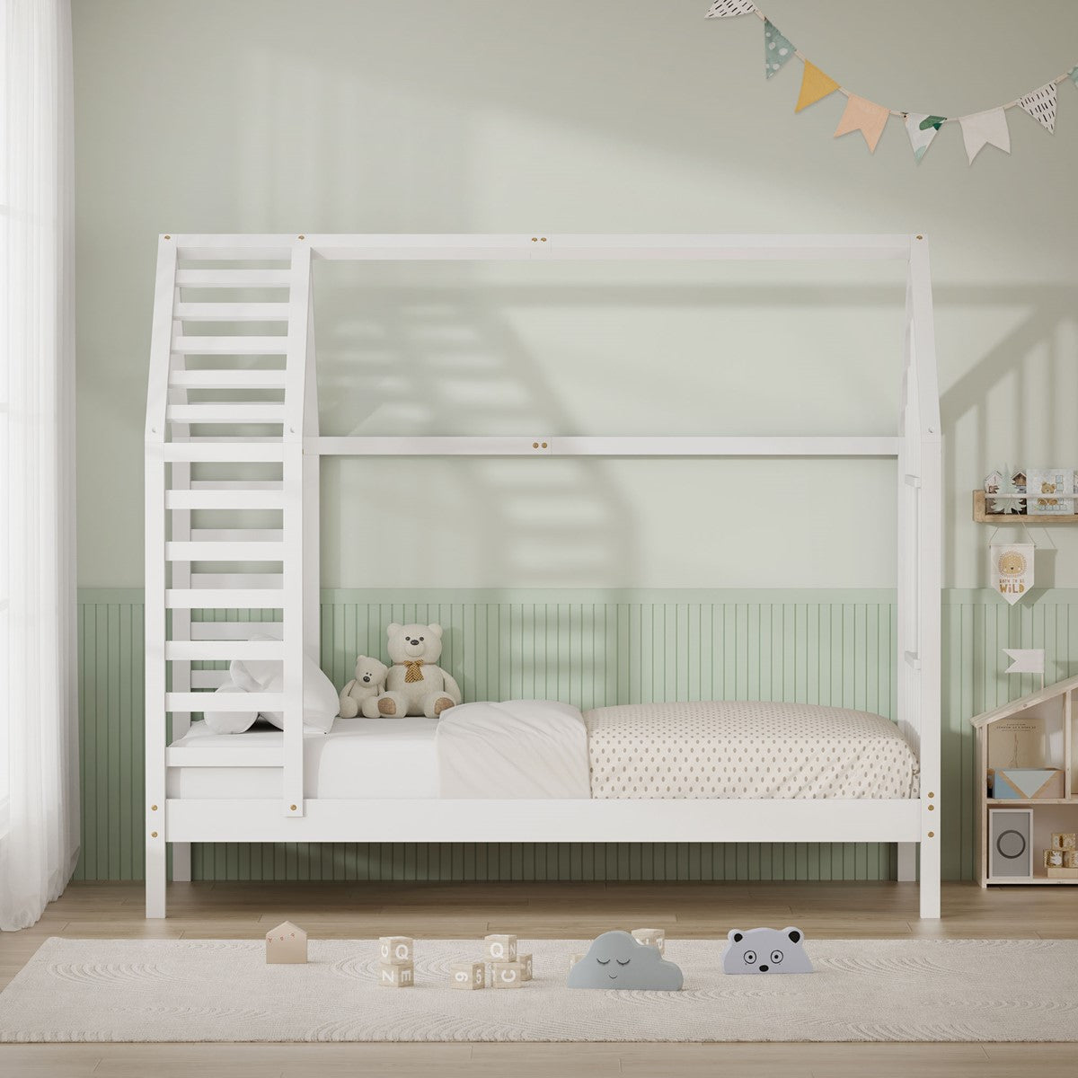 Weißes Holz-Kinderbett in Hausform mit Kissen und Spielzeug auf der Matratze.