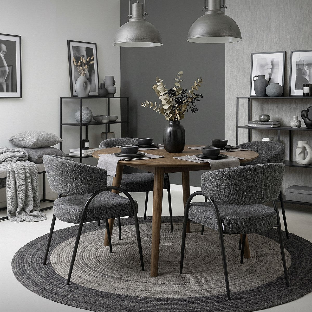 Vier graue Esszimmerstühle mit schwarzen Gestellen stehen um einen runden Holztisch in einem modern eingerichteten Raum.