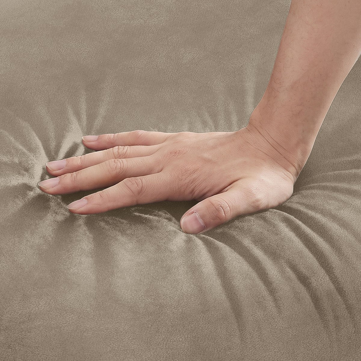 Een hand drukt in de beige, doorgestikte stof van een gestoffeerde zitting.