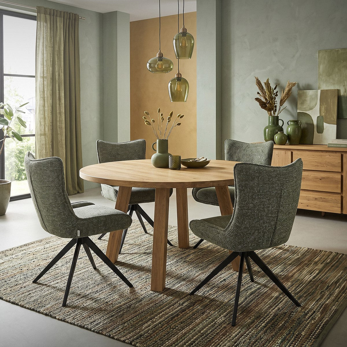 Vier grüne Polsterstühle stehen um einen runden Holztisch in einem Esszimmer.