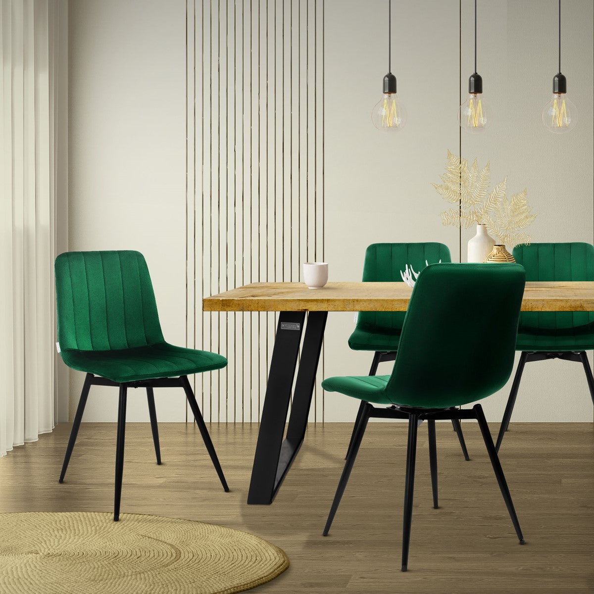 Groene gestoffeerde stoelen met zwarte poten aan een eettafel met een houten blad; erboven hangen drie hanglampen.